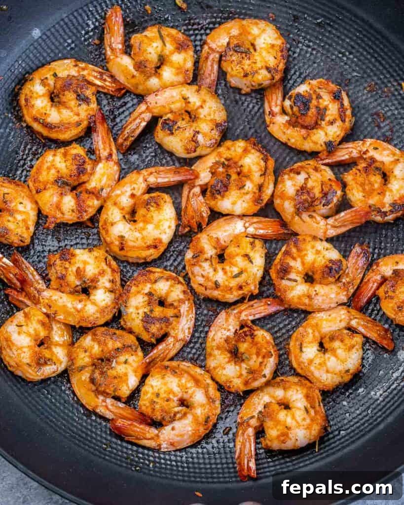 Several seasoned jumbo shrimp are searing to a perfect blackened crust in a large, hot cast iron skillet, creating a delicious aroma.