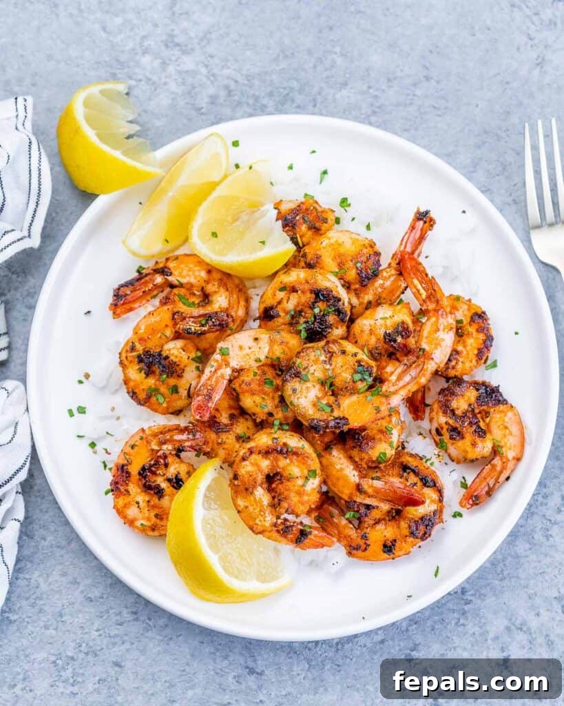 A high-angle view of a circular white plate, beautifully presenting white rice topped with generous portions of blackened shrimp, accompanied by bright lemon wedges for garnish.