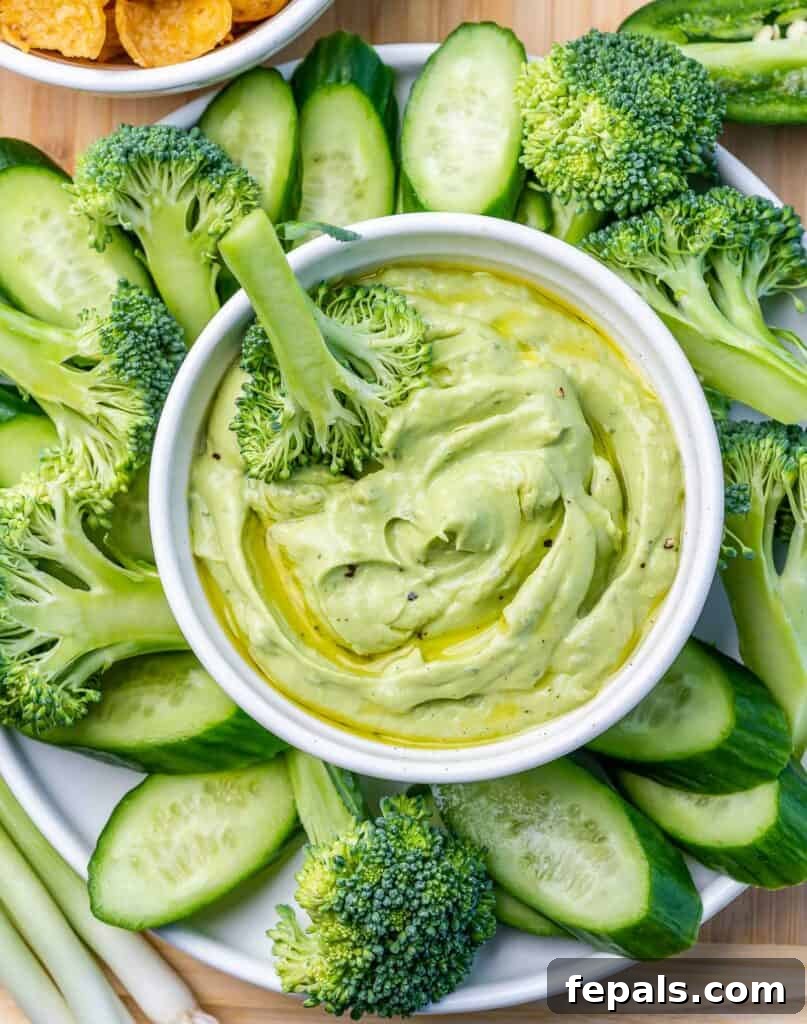 top view of a cutting board with green veggies and an avocado ranch dip in a bowl