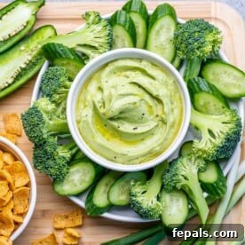 top view green dip made with avocado and yogurt surrounded by slices of cucumbers and broccoli