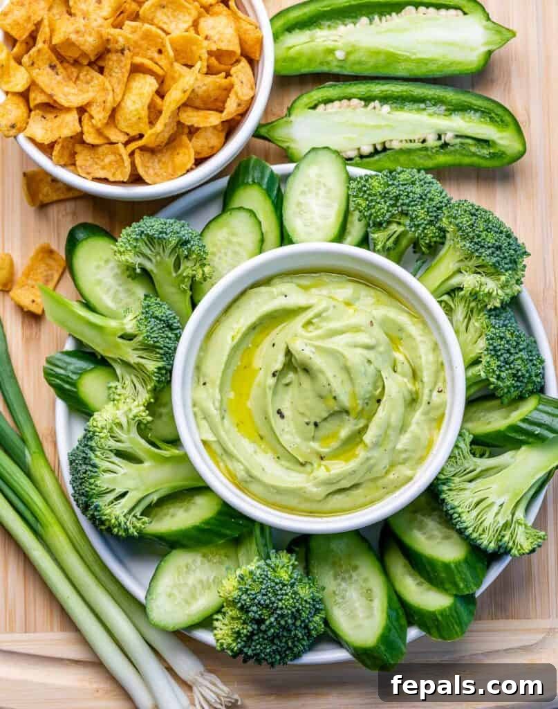 top view of a veggie platter with all green veggies next to a bowl with green avocado dip 