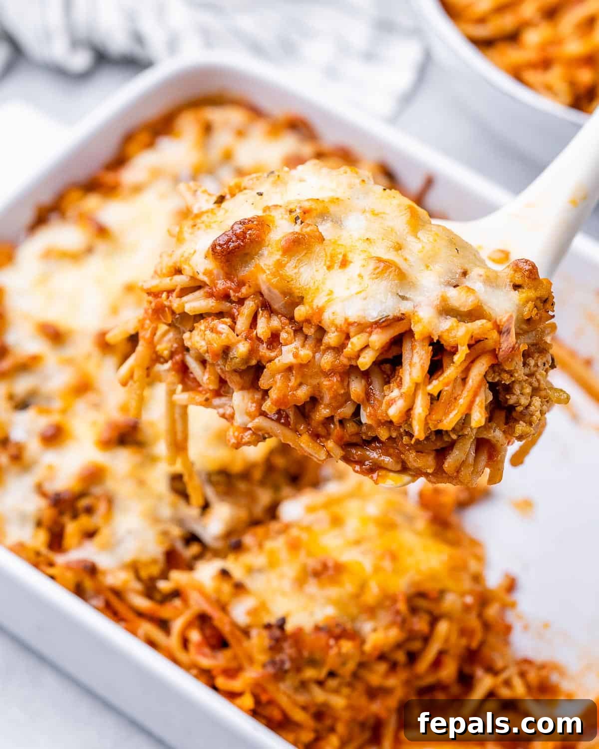 A generous serving of Million Dollar Spaghetti being scooped out of a casserole dish, showing the beautiful layers of pasta, meat sauce, and melted cheese.
