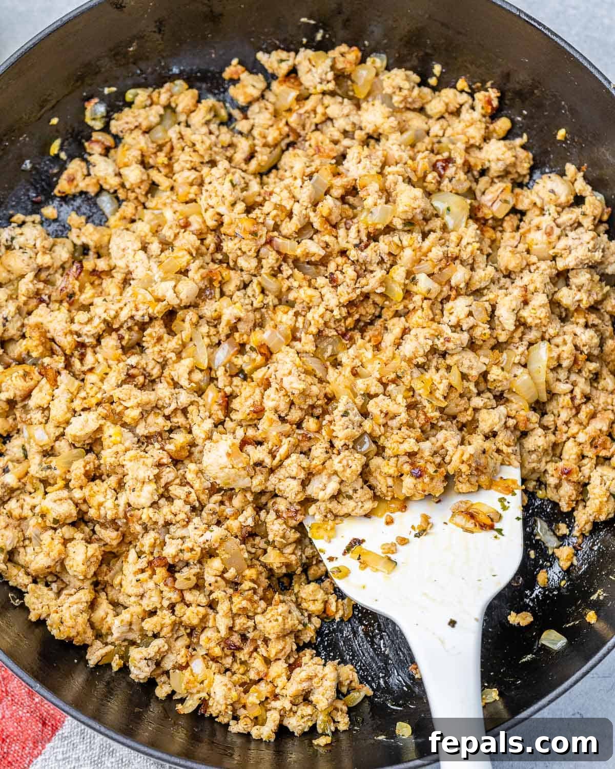 Browning ground chicken or turkey in a skillet with onions and garlic, part of the Million Dollar Spaghetti preparation.