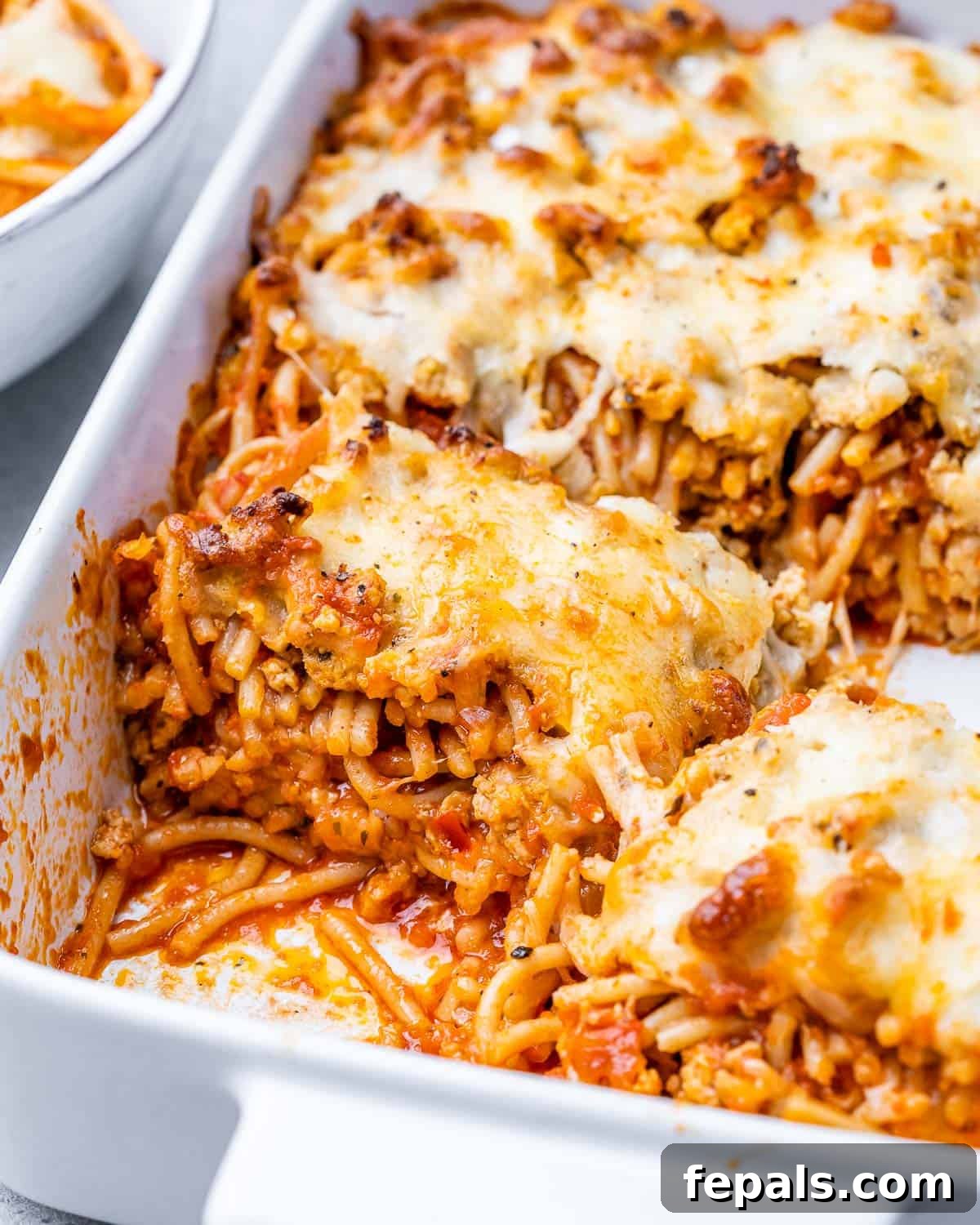 Million Dollar Spaghetti beautifully assembled in a white casserole dish, topped with shredded mozzarella before baking.