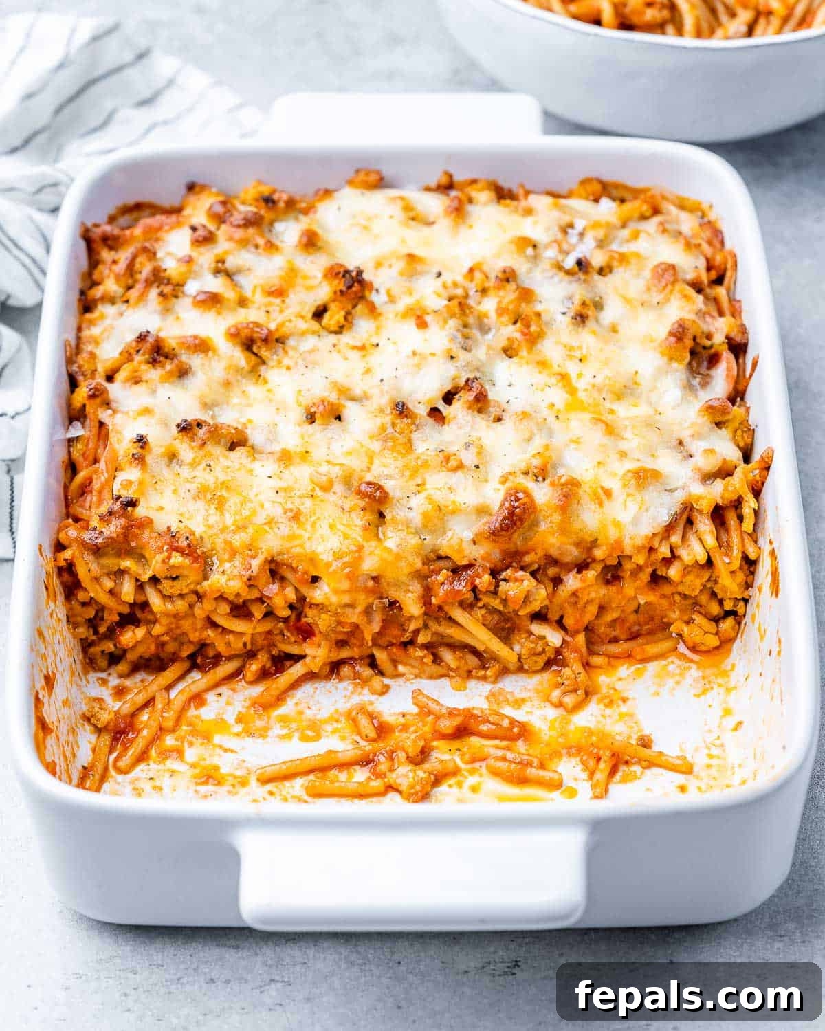 A delicious side shot of Million Dollar Spaghetti in a white baking dish, showing rich red sauce and melted golden cheese on top.