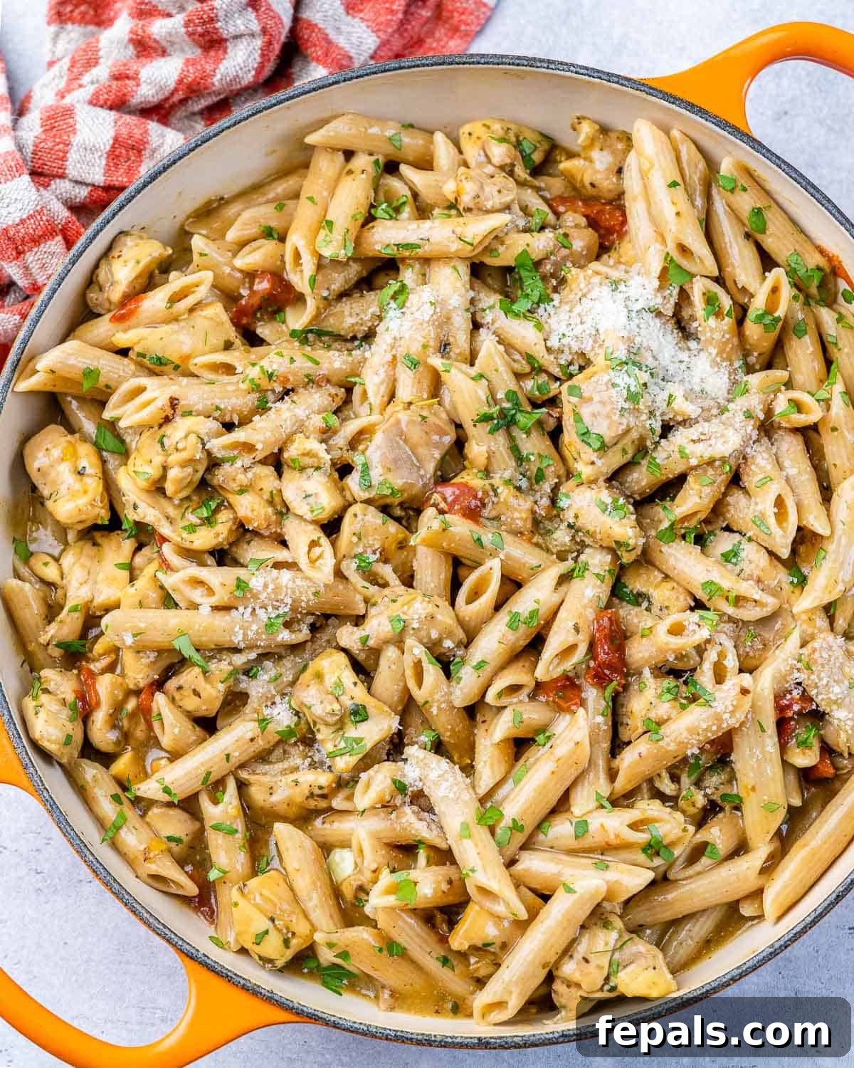 Top view of creamy Marry Me Chicken Pasta with penne in an orange skillet, garnished with fresh parsley.
