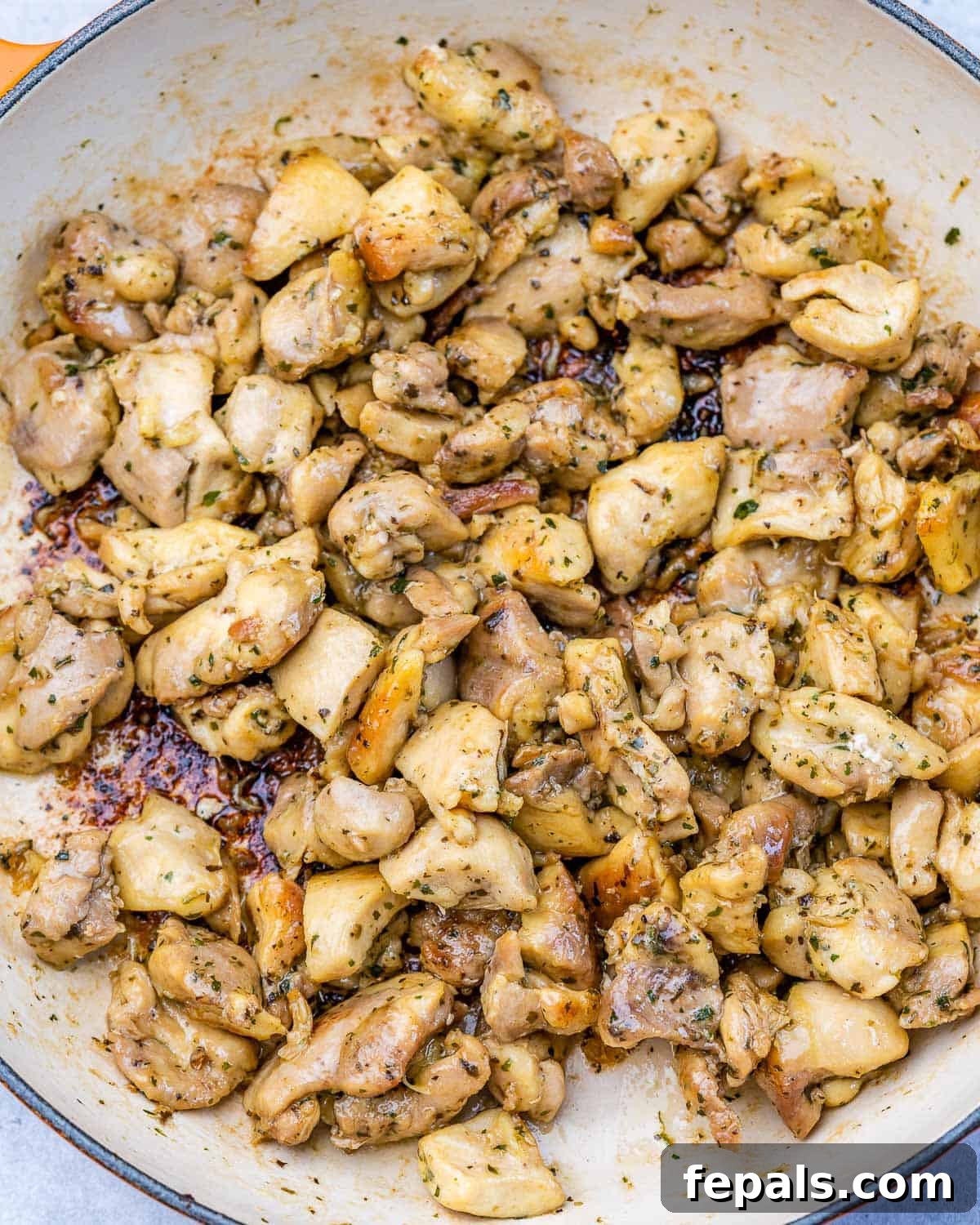 Golden brown, cooked chicken thigh pieces resting in a pan, seasoned with Italian herbs.