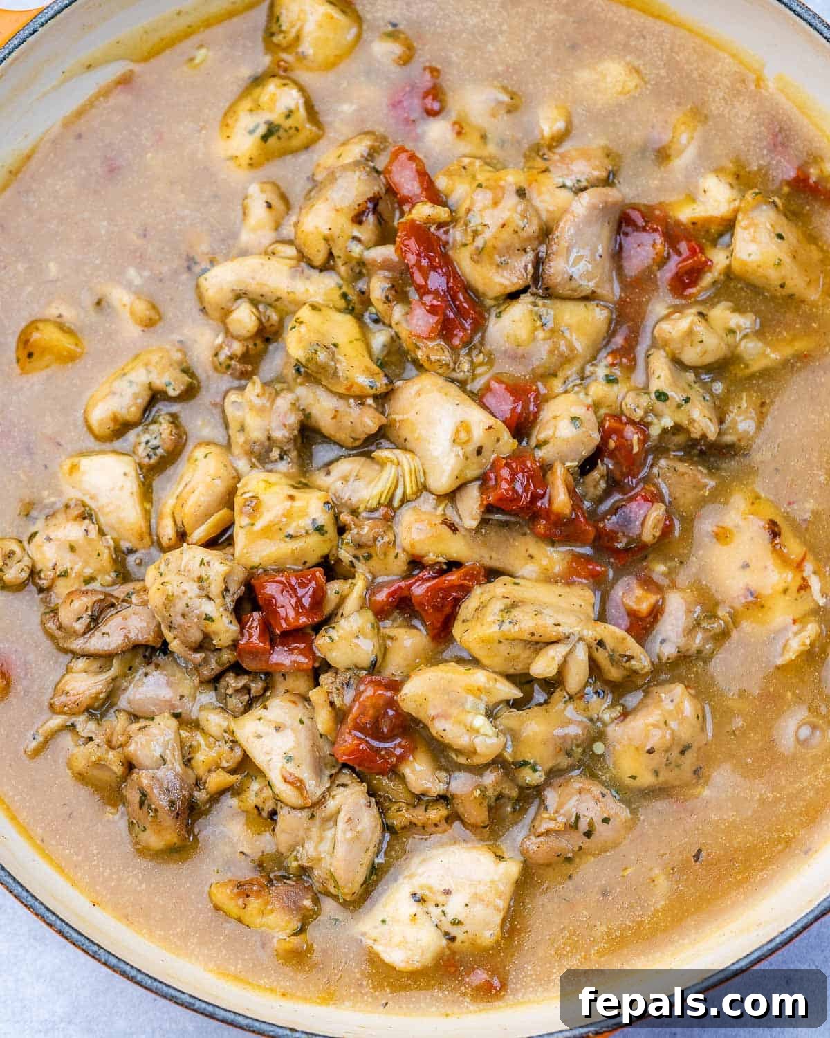 Cooked chicken bites added back into a rich, creamy Tuscan-style sauce with sun-dried tomatoes in a skillet.