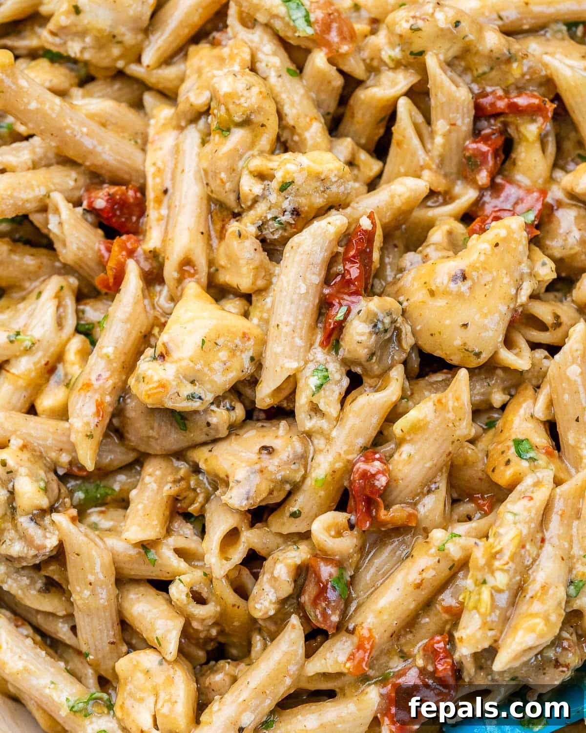 Close-up view of a serving of creamy Marry Me Chicken Pasta with penne, chicken, and sun-dried tomatoes in a skillet, garnished with herbs.