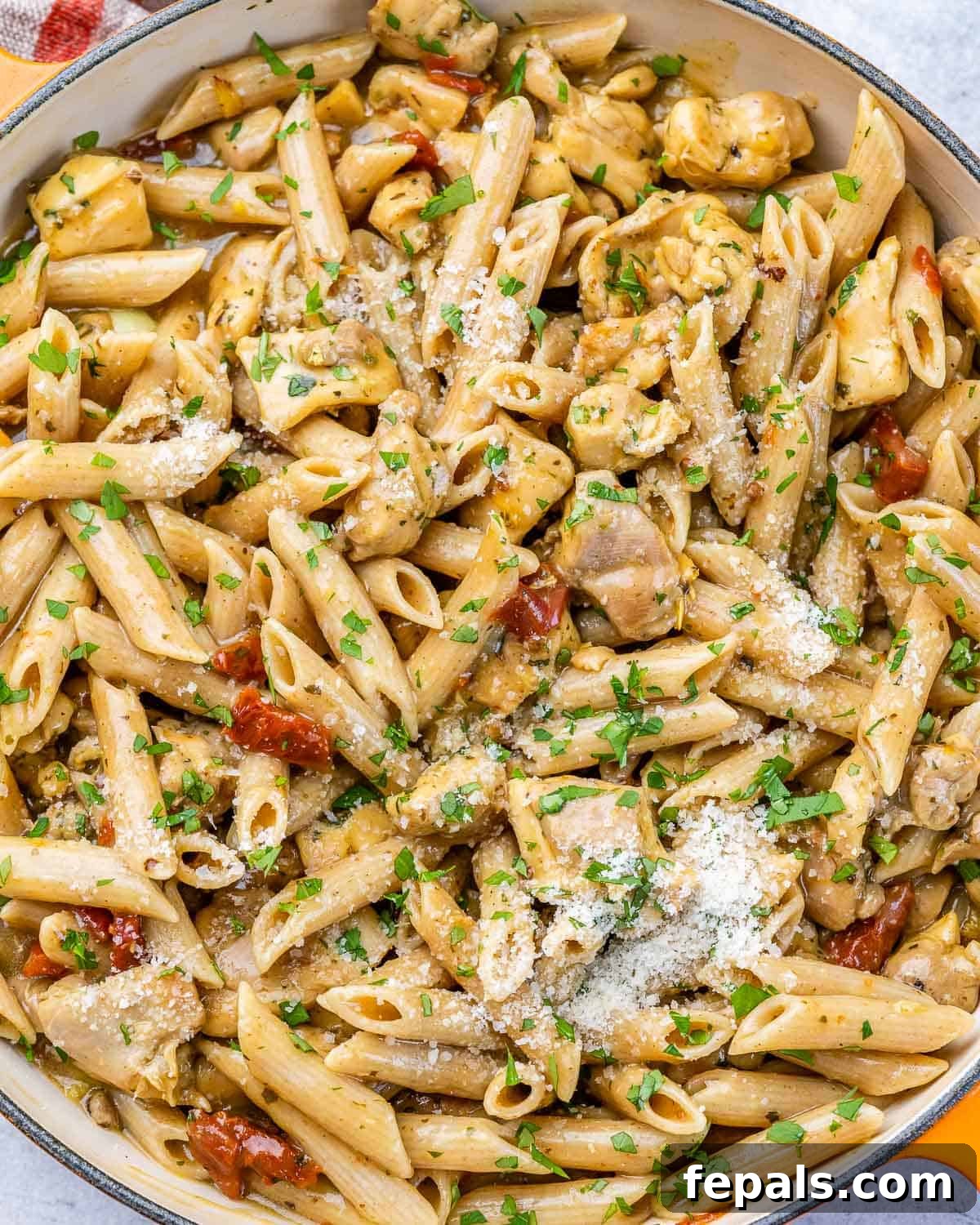 Top view of creamy chicken pasta in a pan, generously garnished with fresh Parmesan cheese and herbs.