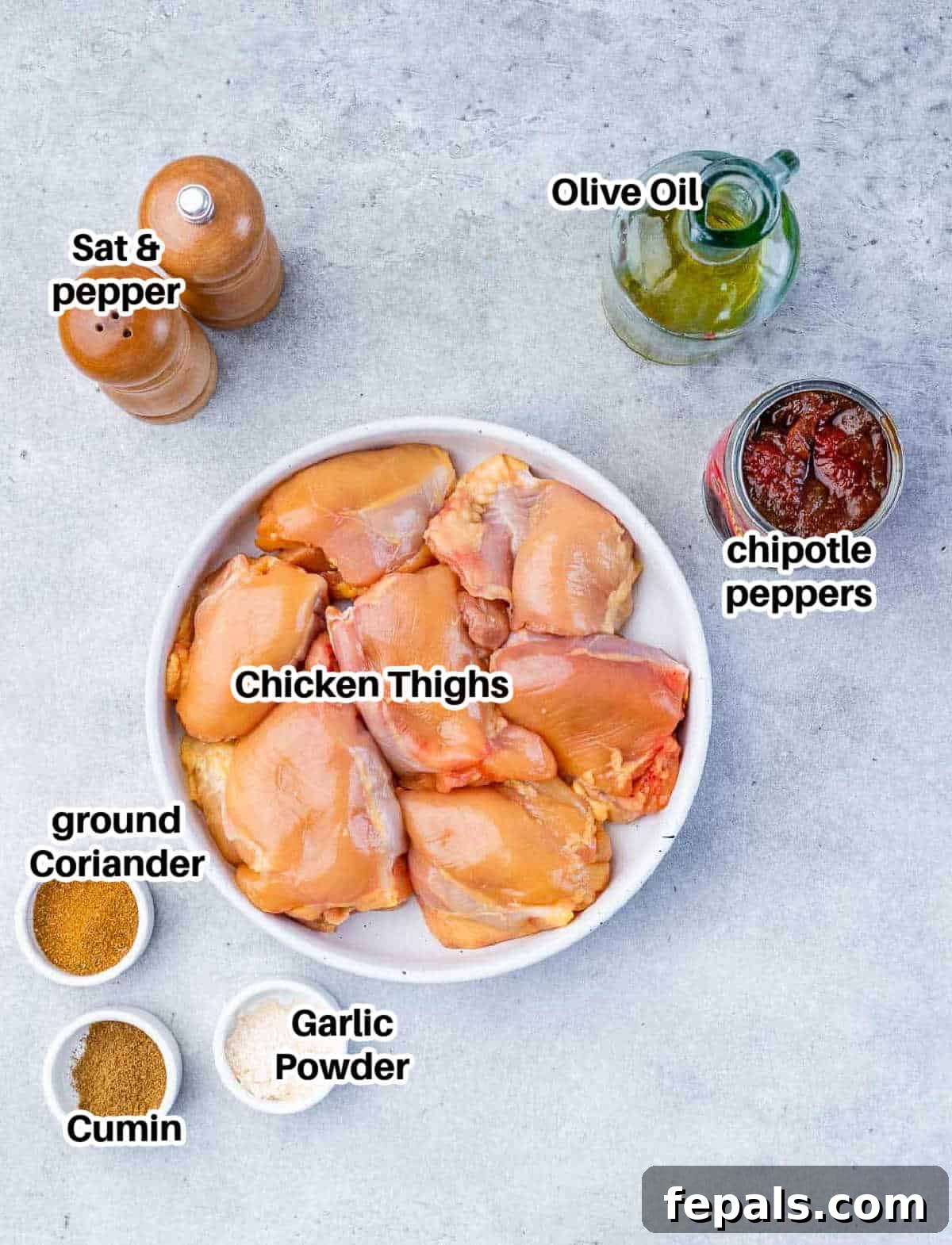 Smoky Chipotle Al Pastor Chicken 3 A vibrant collection of ingredients laid out on a clean surface, including a can of chipotle peppers, various spices, fresh chicken thighs, and olive oil, ready for making Chicken Al Pastor.