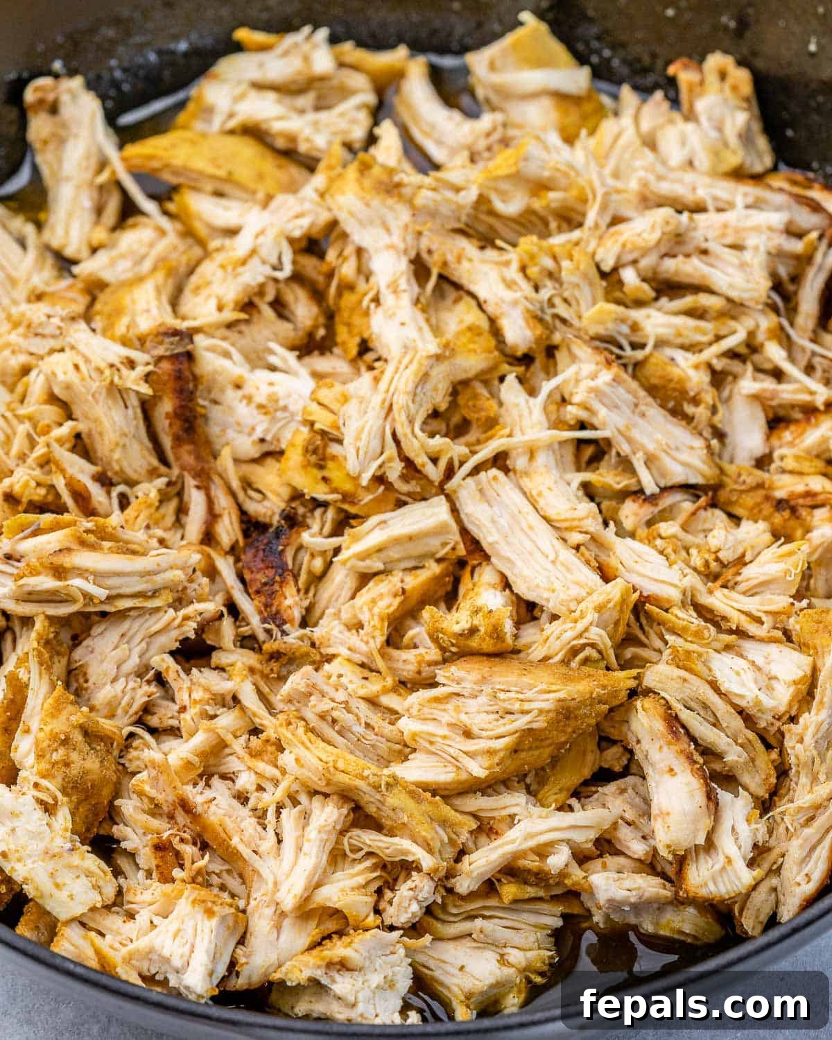 The Ultimate Chicken Tinga 4 Shredded chicken cooking in a pan, absorbing the remaining savory broth before other ingredients are added.