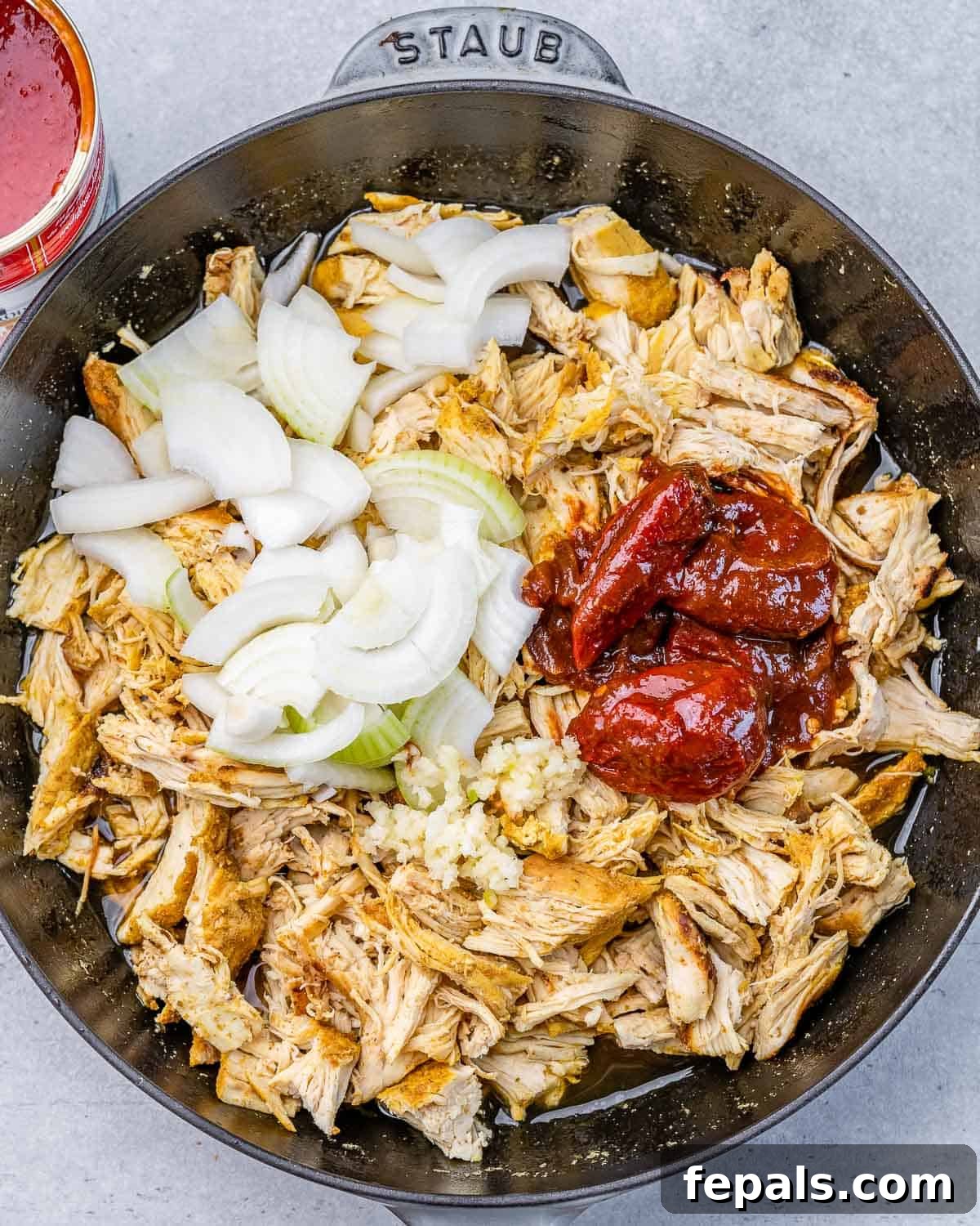 The Ultimate Chicken Tinga 5 Adding vibrant chipotle peppers and aromatic sliced onions to the shredded chicken in the skillet, beginning to build the rich Tinga sauce.