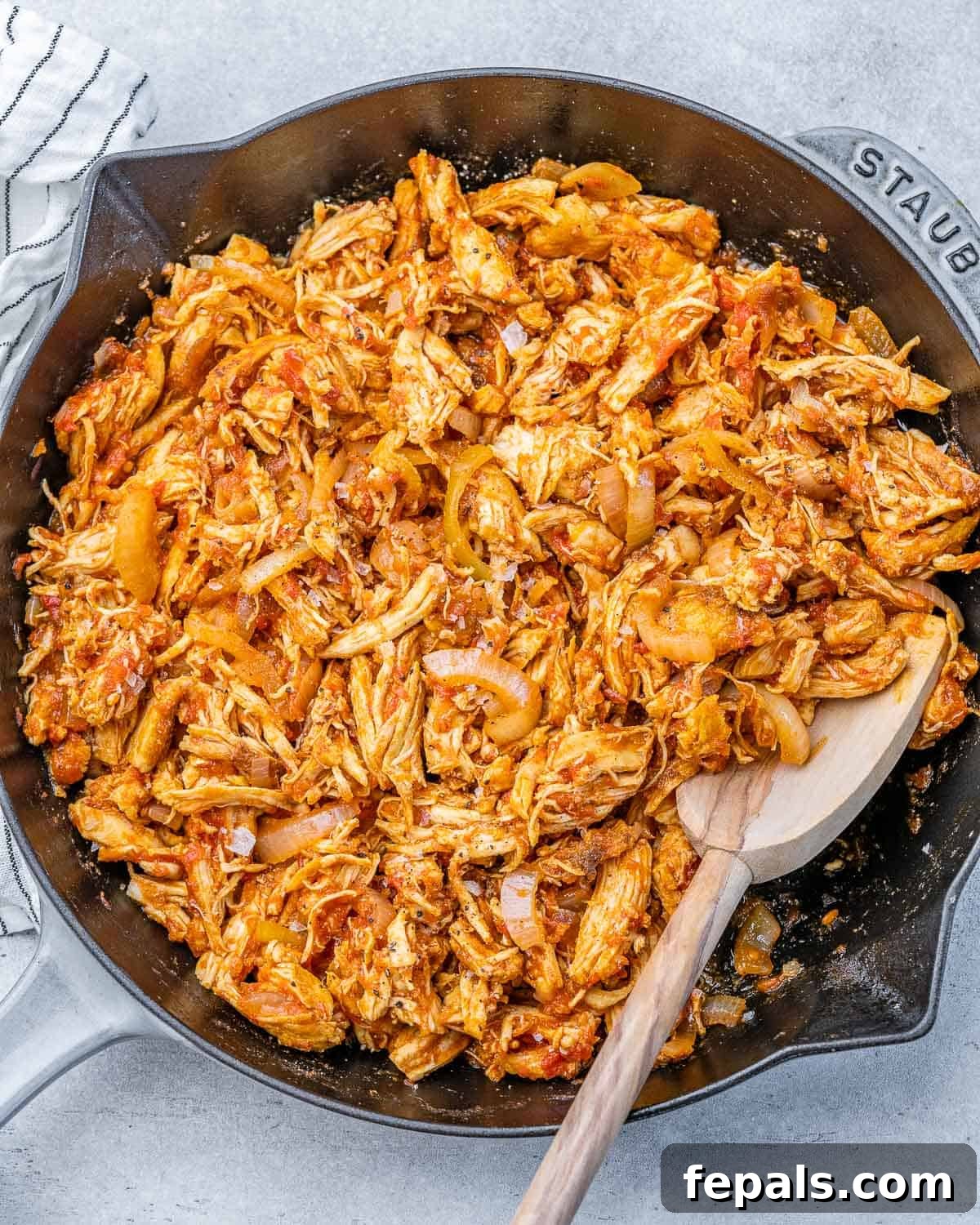 The Ultimate Chicken Tinga 6 A wooden spoon stirring saucy shredded chicken in a large skillet, showcasing the rich, uniform coating of the Tinga sauce.