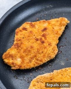 Breaded chicken cutlet cooking in a skillet until golden brown and crispy on the edges.