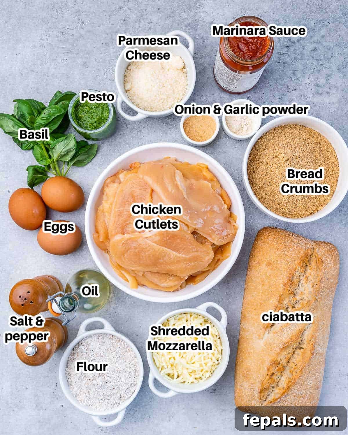 Crispy Chicken Parmesan Sandwich Outshines Takeout 3 A flat lay photograph of all the fresh ingredients needed for a chicken parmesan sandwich, including chicken breasts, seasonings, flour, eggs, breadcrumbs, cheeses, marinara, pesto, and ciabatta bread.