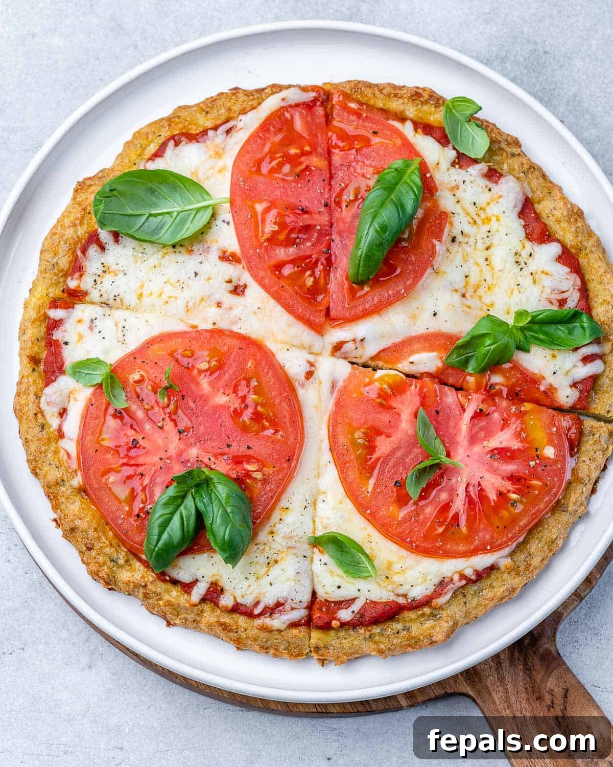 Savory chicken crust pizza adorned with melted mozzarella, ripe tomato slices, and fresh green basil leaves, presented on a pristine white plate, ready to be enjoyed.