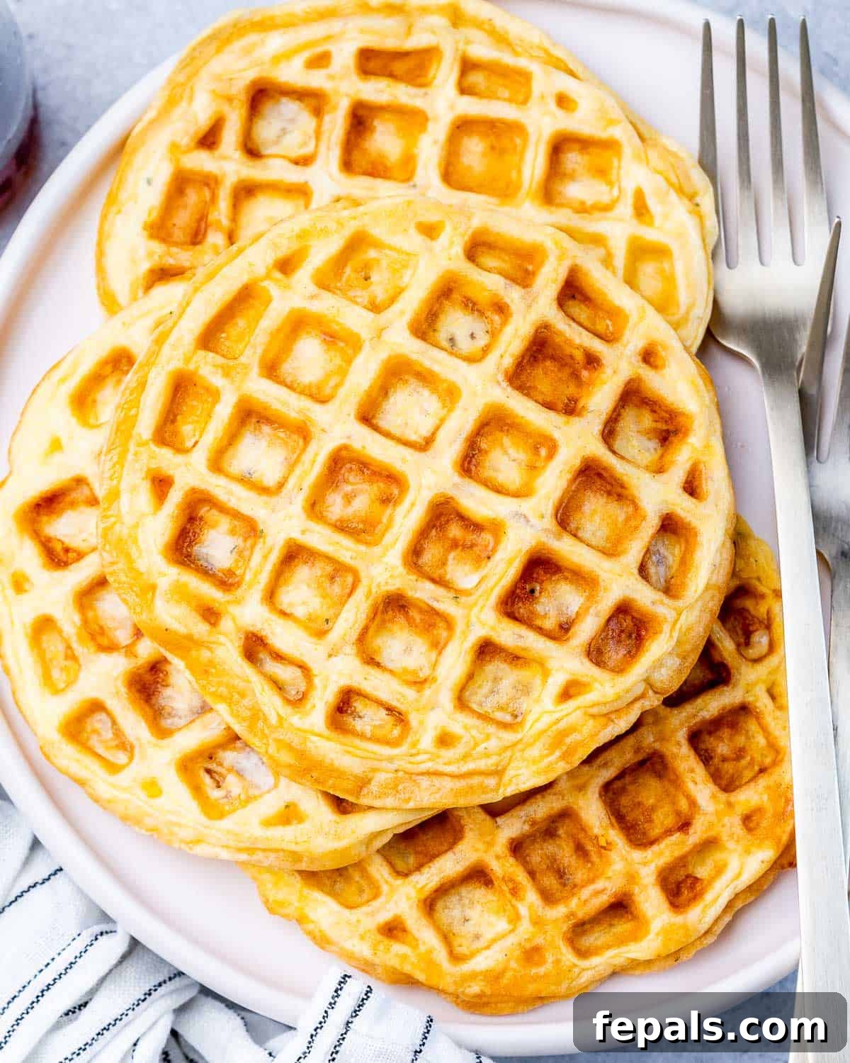 A stack of three golden-brown chaffles on a white plate with a fork on the side, ready to serve.