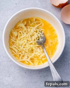 A white bowl with a fork stirring the chaffle batter, made of whisked egg, shredded mozzarella, and garlic salt.