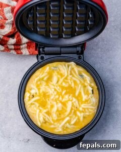 A waffle maker in mid-cook, filled with chaffle batter made of egg and cheese.
