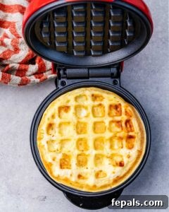A mini waffle maker opened to show a fully cooked, golden chaffle inside.