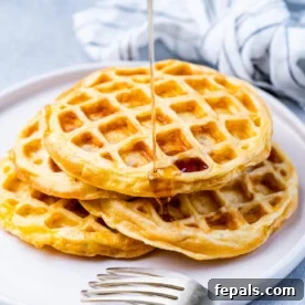 A plate with four chaffles piled high, lightly overlapping, with a gray napkin and silver fork nearby.