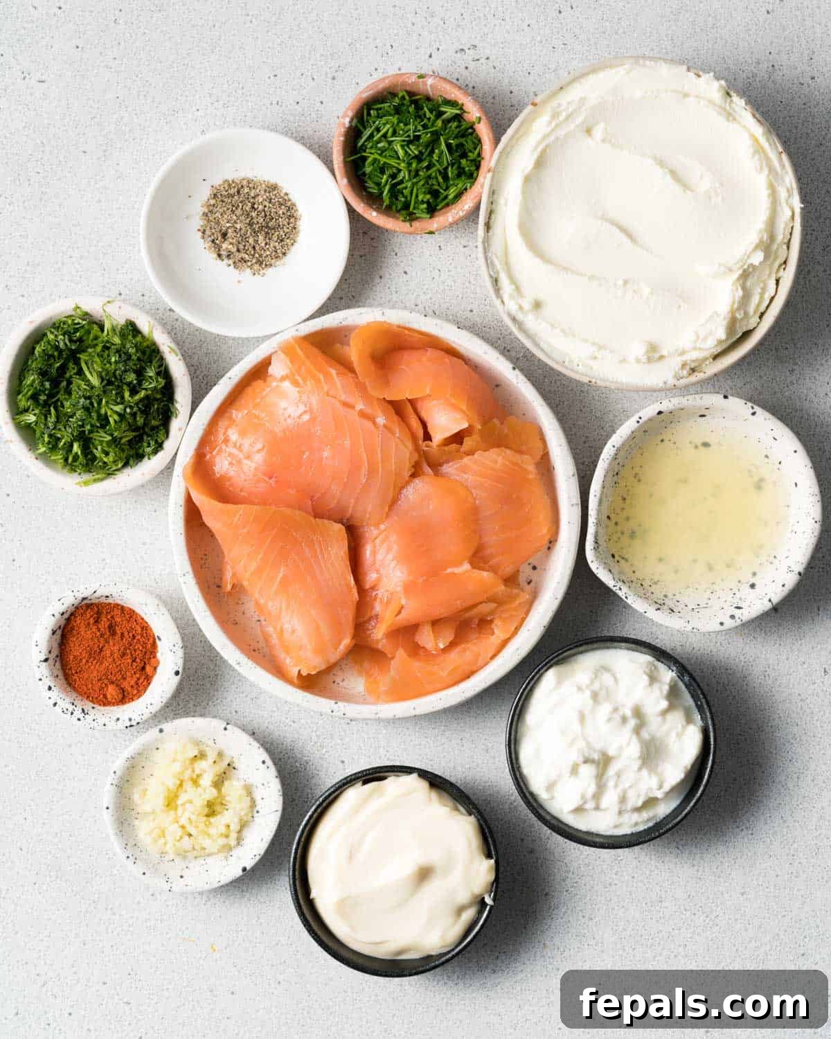 Smoked salmon in a bowl with small bowls of mayo, sour cream, cream cheese, lemon juice, dill and spices.