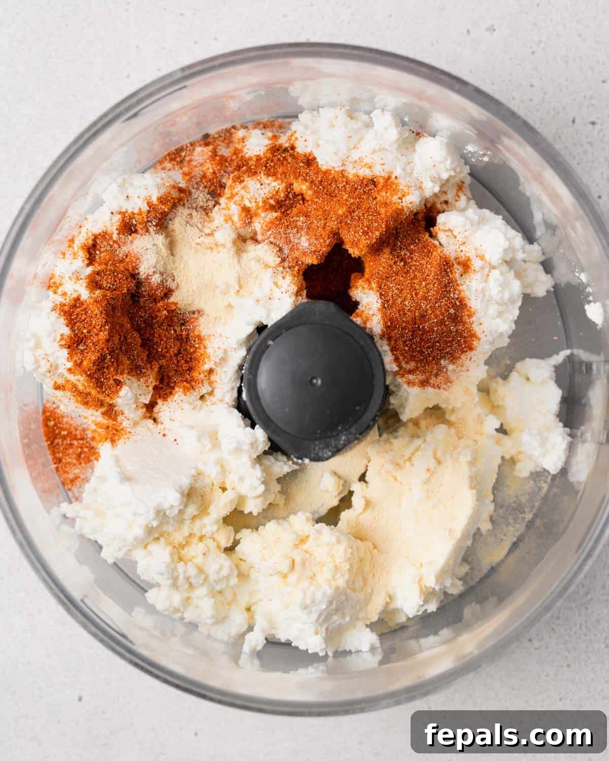 The Creamy Cottage Cheese Queso Hack 5 Cottage cheese being added to a food processor with taco seasoning sprinkled on top, ready for blending.