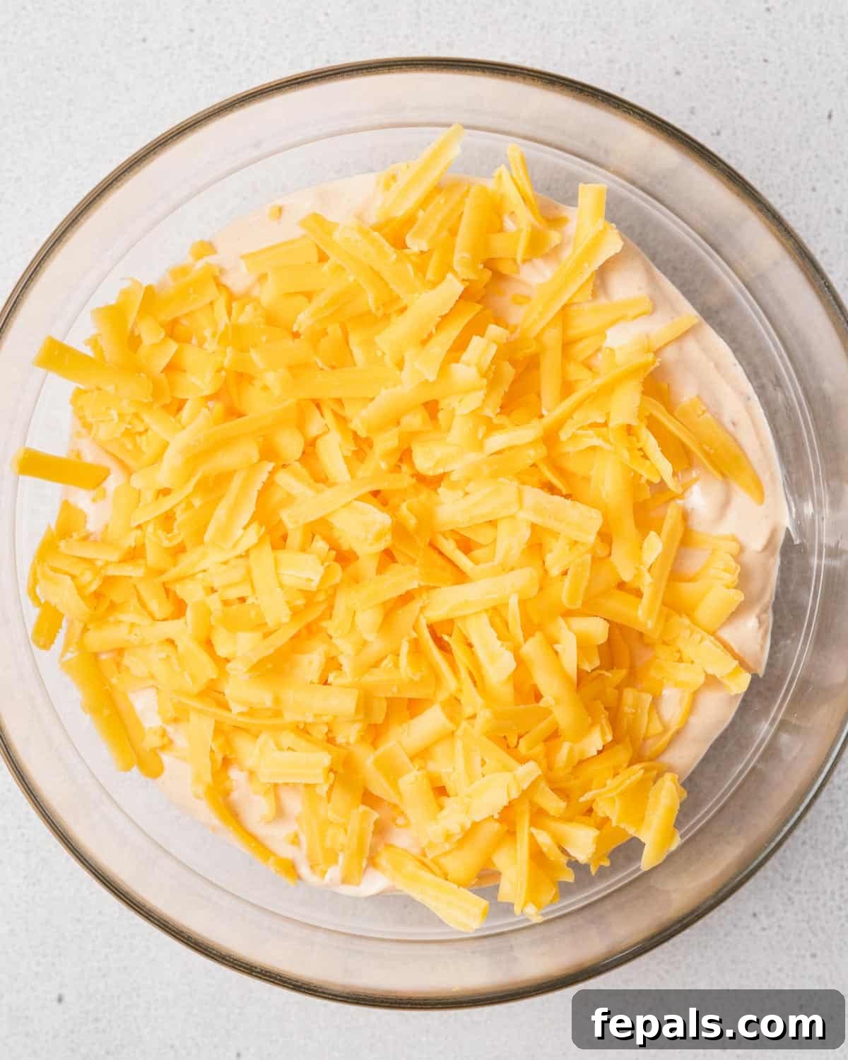 The Creamy Cottage Cheese Queso Hack 8 Shredded cheddar cheese layered on top of the blended cottage cheese in a bowl, prepared for heating.