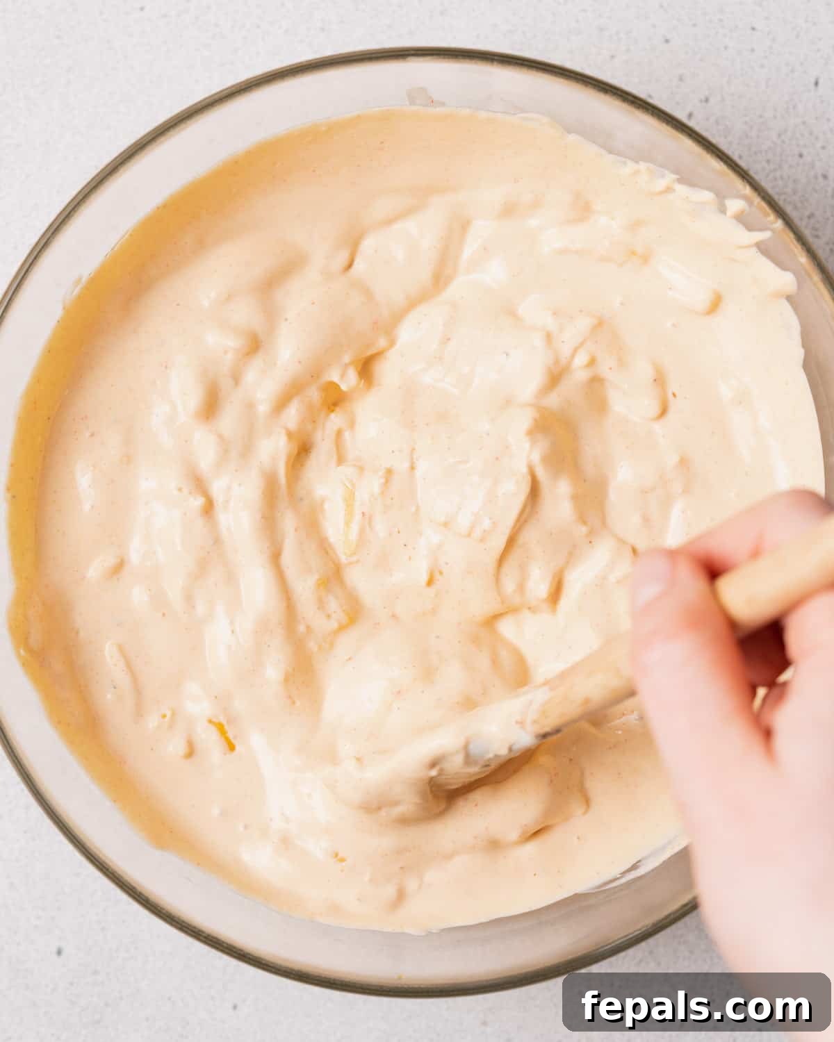 The Creamy Cottage Cheese Queso Hack 9 A spoon actively stirring the melted shredded cheese and cottage cheese together in a bowl, ensuring a uniform and creamy consistency.