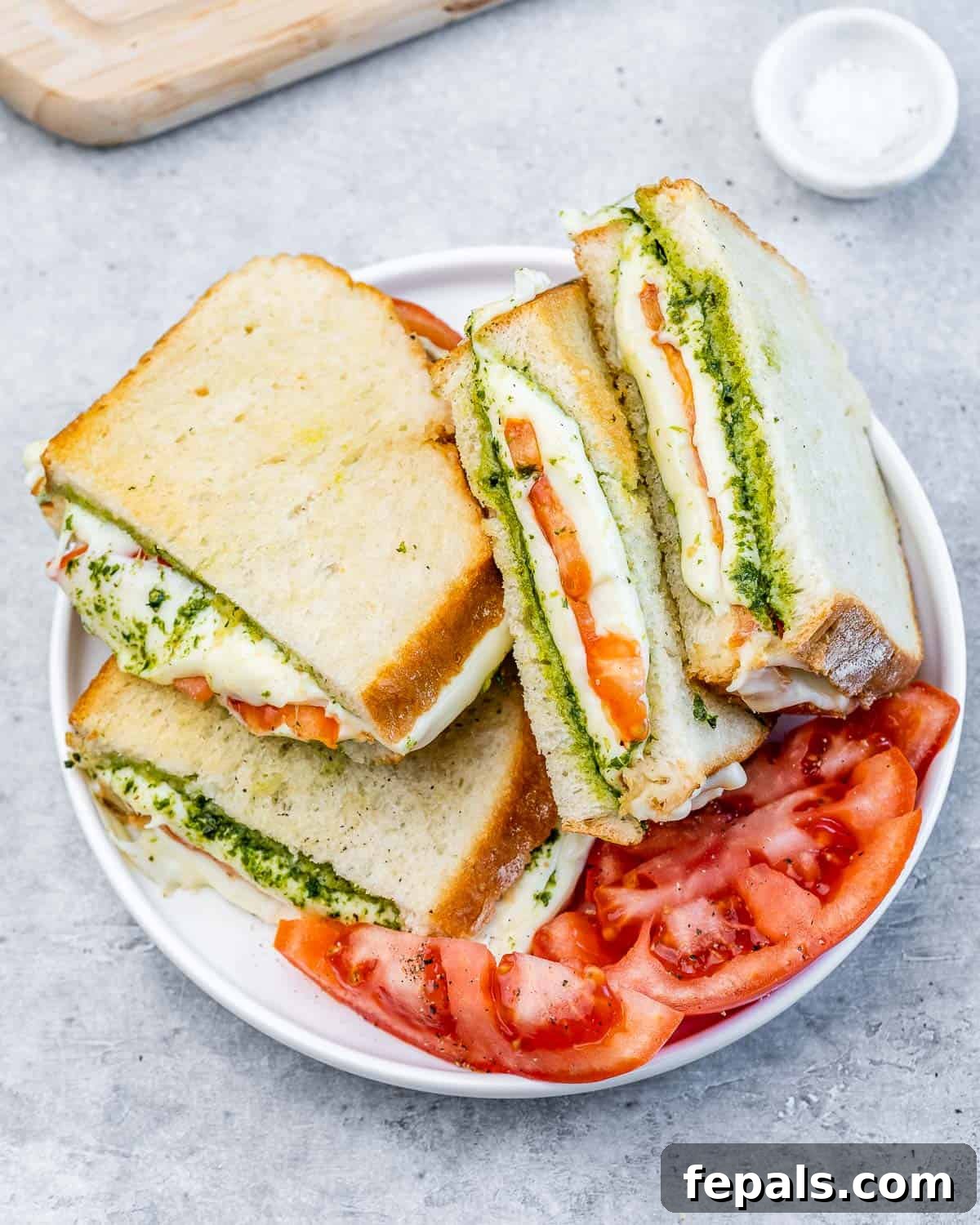 Air fryer grilled cheese sandwich on a white plate with tomato slices. The sandwich is perfectly golden brown and slightly cut open to show the melted cheese and fresh tomato.
