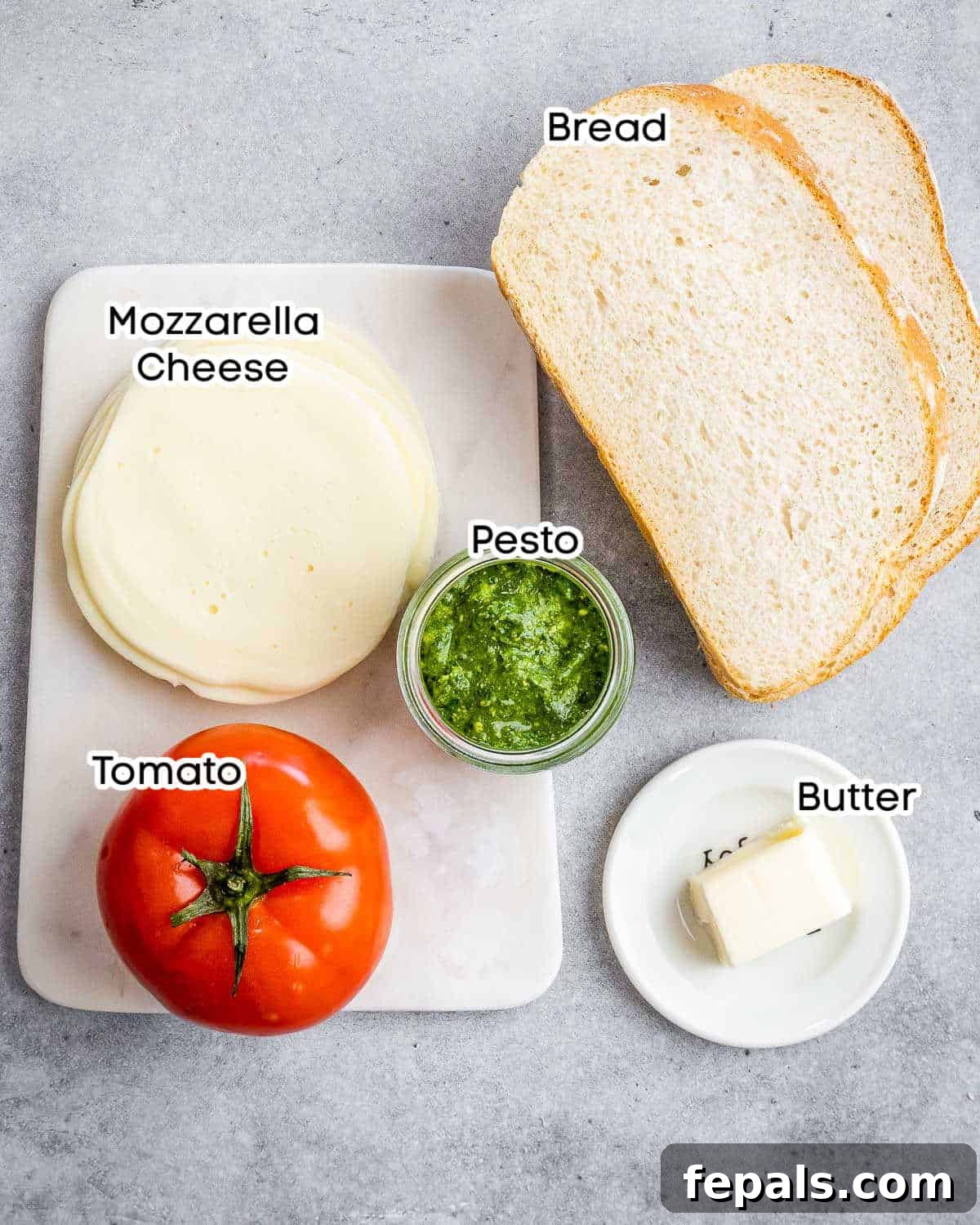 ingredients to make grilled cheese with pesto and tomatoes including bread, butter, pesto, mozzarella, and sliced tomatoes.