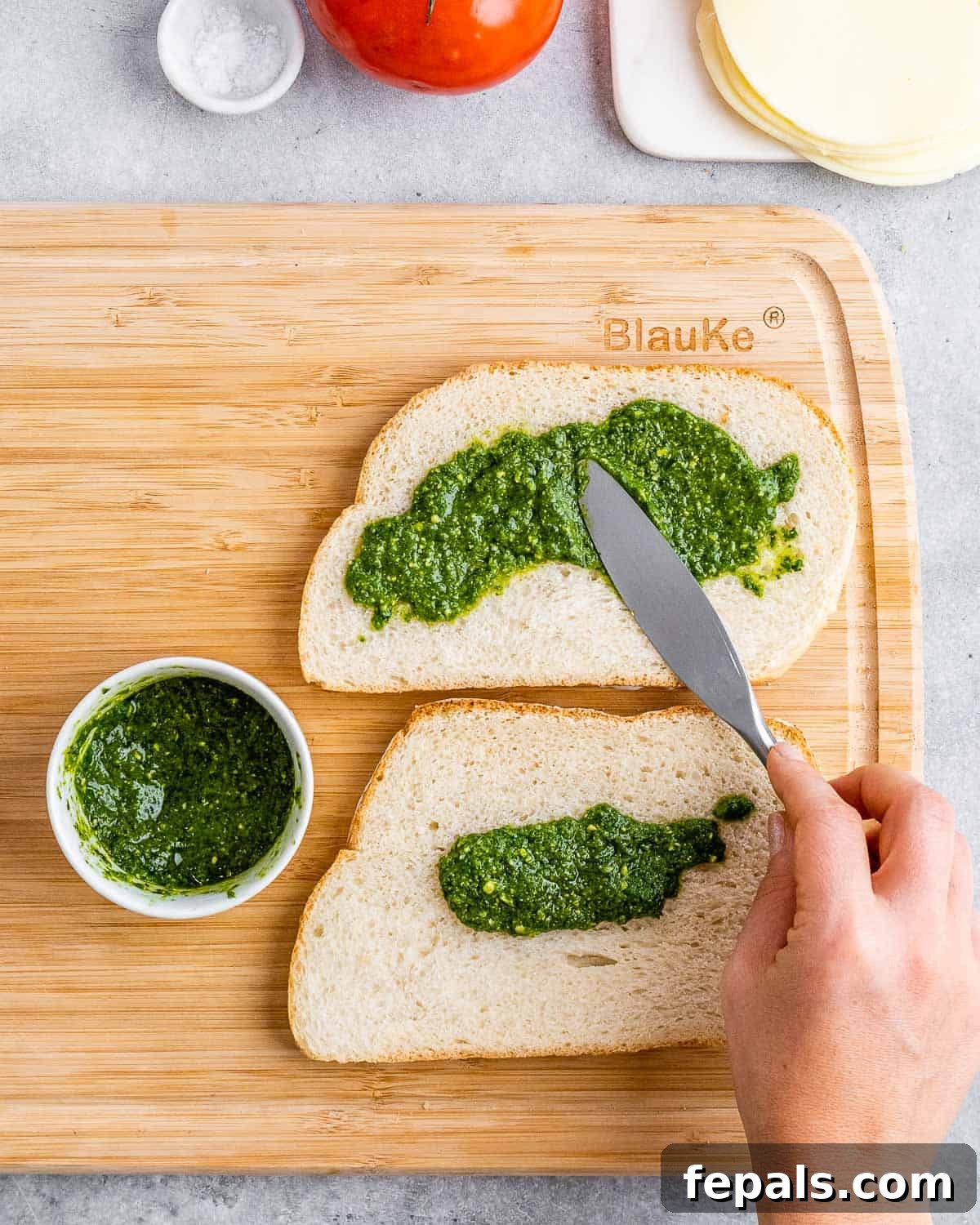 Spreading fragrant basil pesto over the unbuttered side of sliced bread.