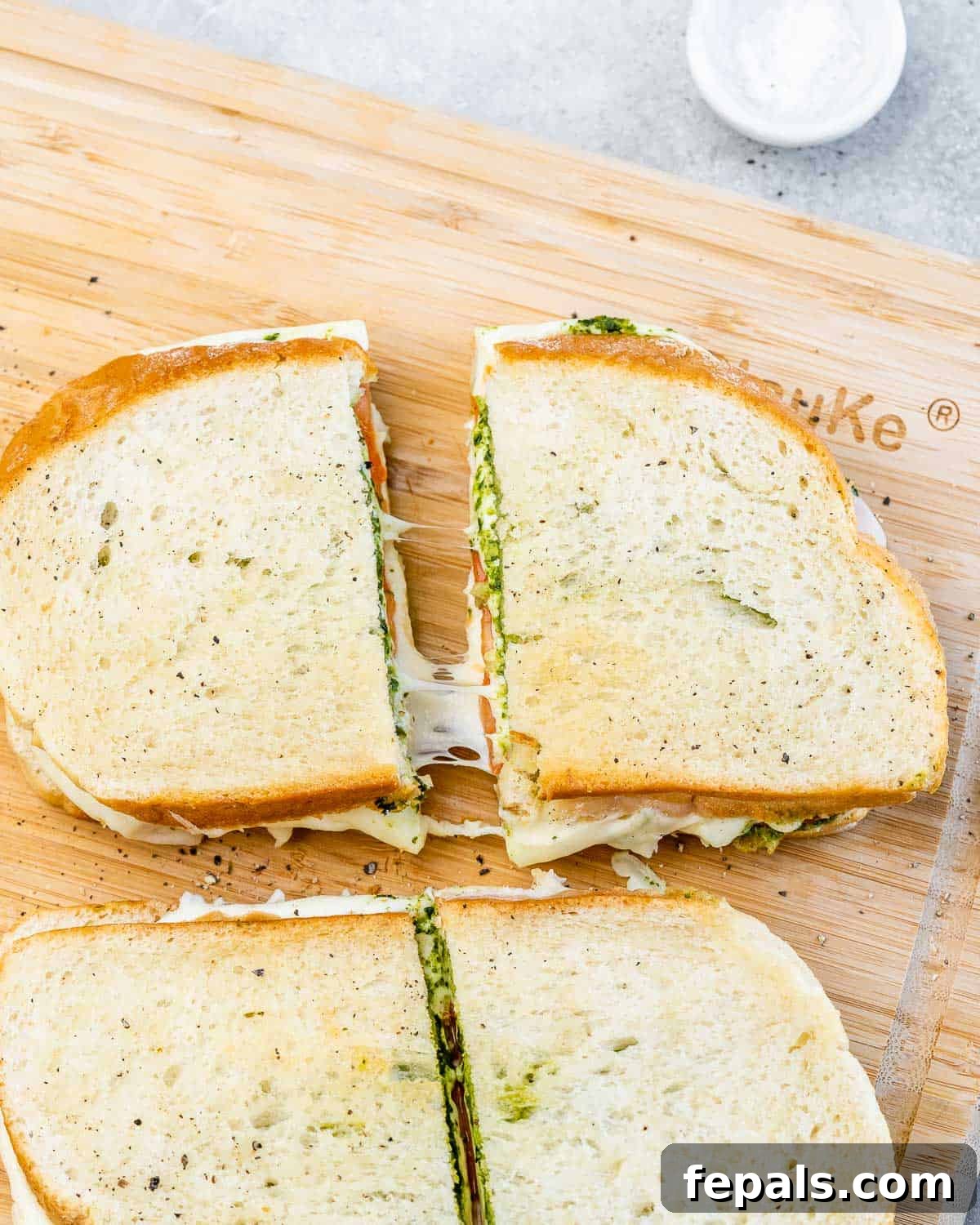 A perfectly golden air fryer grilled cheese sandwich, sliced in half on a wooden cutting board, revealing the melted cheese, pesto, and tomato.