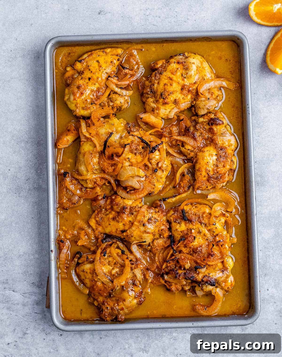 Marinated chicken thighs cooking on a large sheet pan, their juices bubbling around them in the oven.