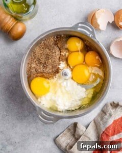 Eggs, cottage cheese, and oil added over blended oats in a food processor, ready to be combined into a smooth batter.