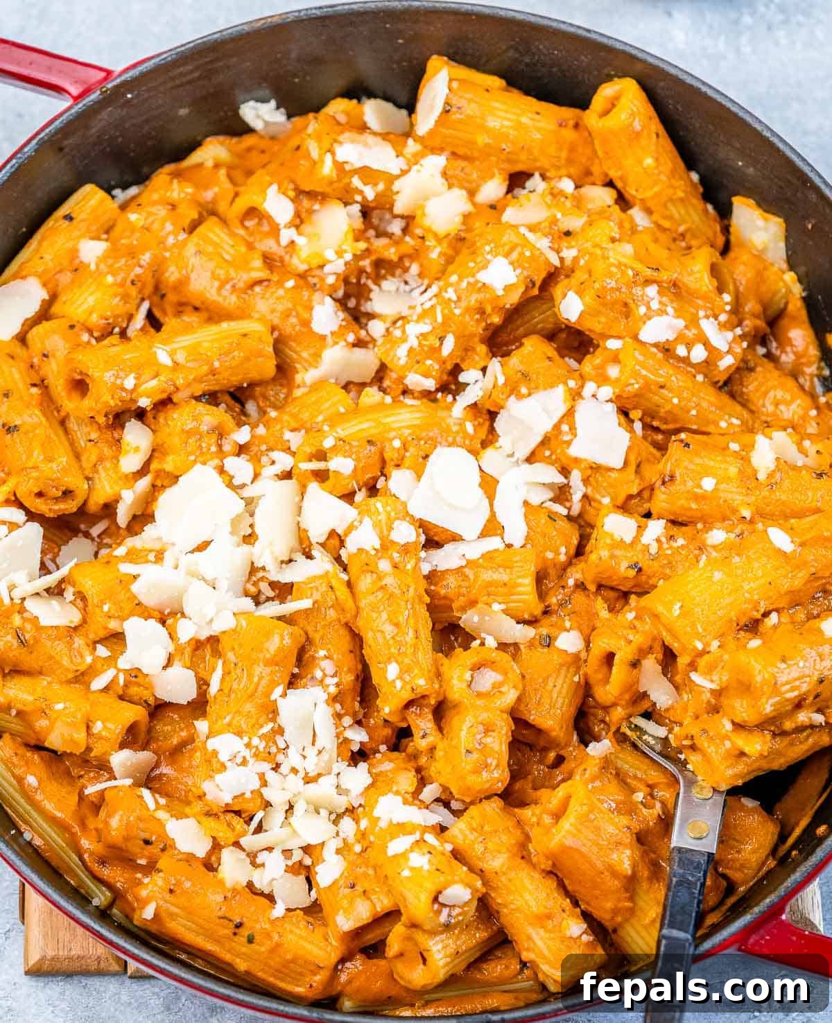 A vibrant red skillet holds creamy tomato-based pasta, generously topped with shredded Parmesan cheese and fresh basil leaves, ready to be served.