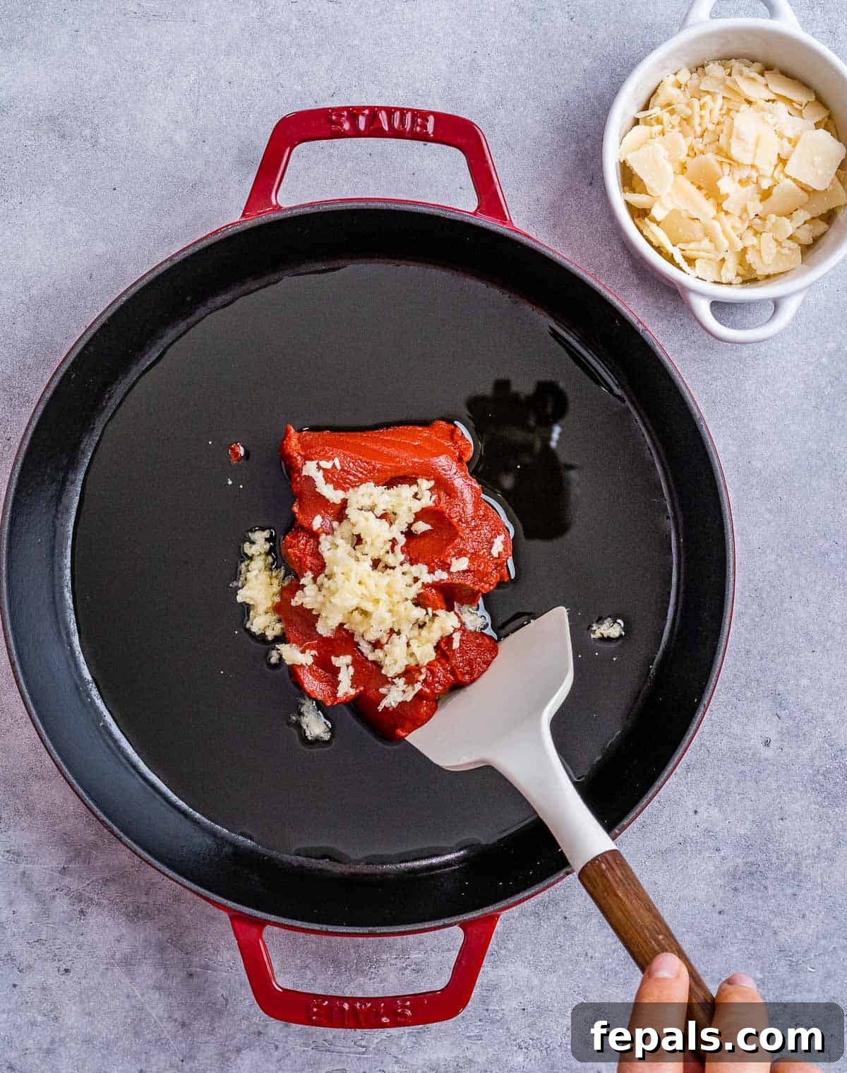 Sautéing tomato paste and minced garlic in olive oil in a skillet, creating an aromatic base for the sauce.