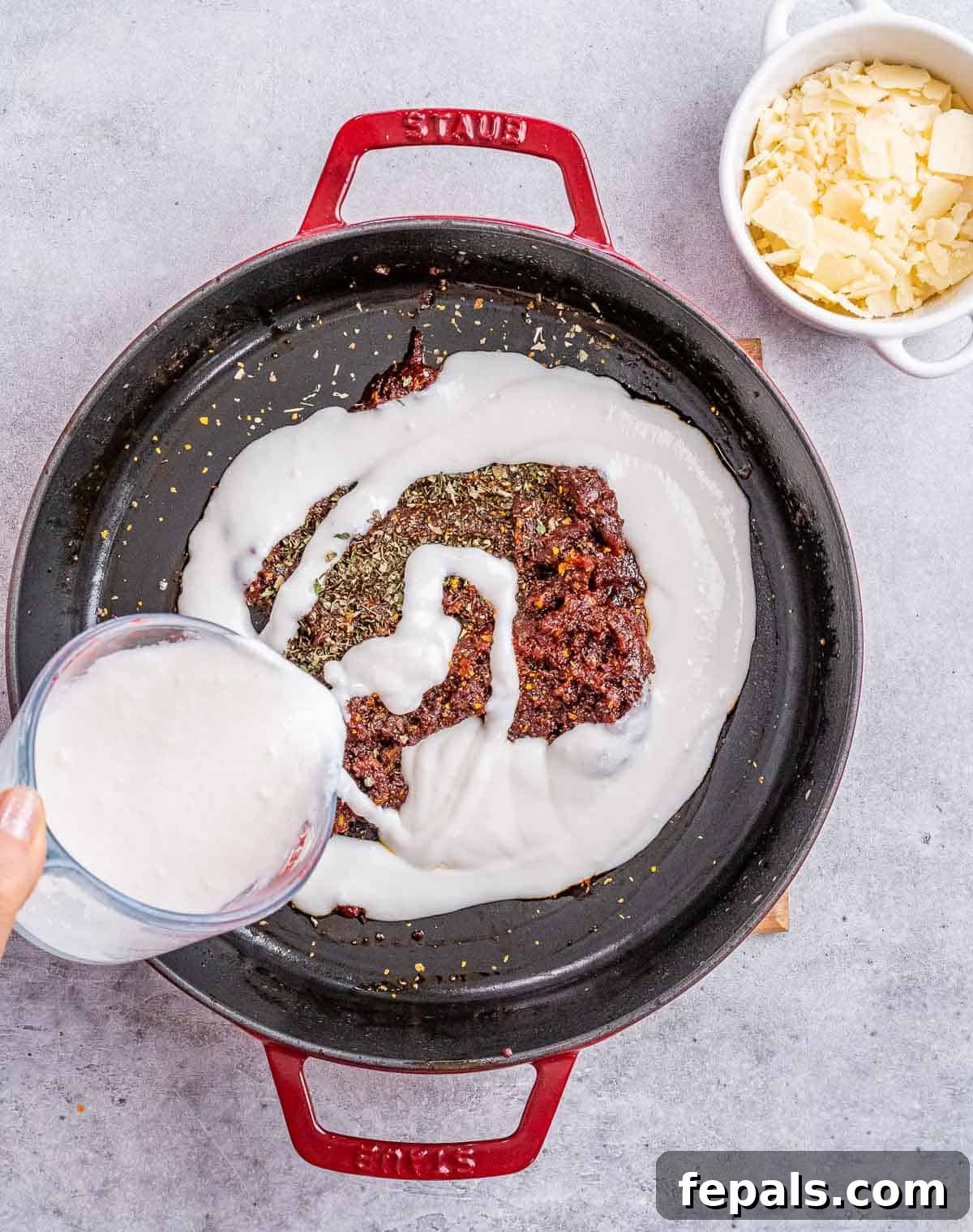 Pouring creamy coconut milk into the cooked tomato paste and olive oil mixture in a skillet, beginning to form the luscious sauce.