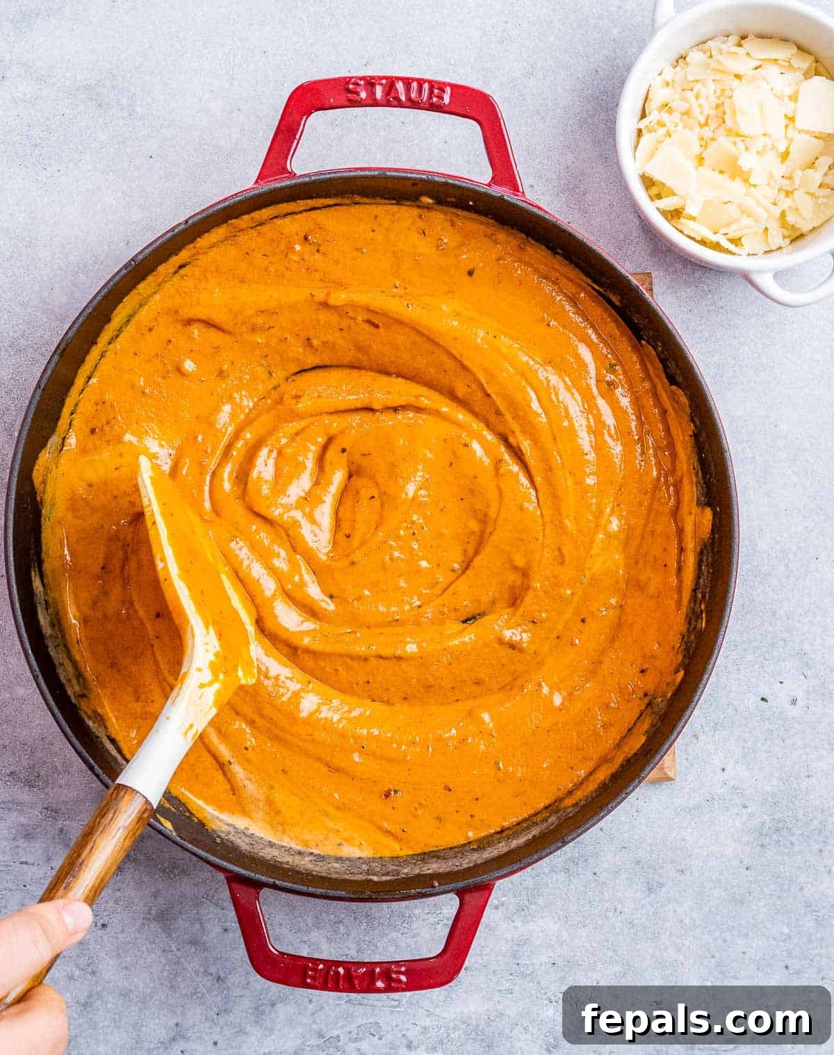 Stirring in reserved pasta water into the simmering creamy tomato sauce, adjusting its consistency.