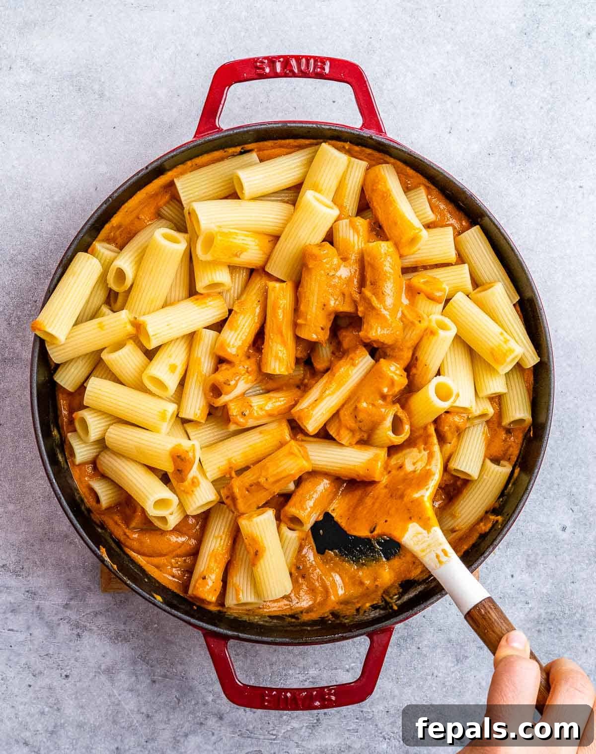 Tossing cooked pasta vigorously in the creamy tomato sauce within a large skillet, ensuring every noodle is perfectly coated.