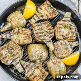 Smoky Grilled Artichoke Halves 11 A grill pan with grilled artichoke halves with lemon garnishes.
