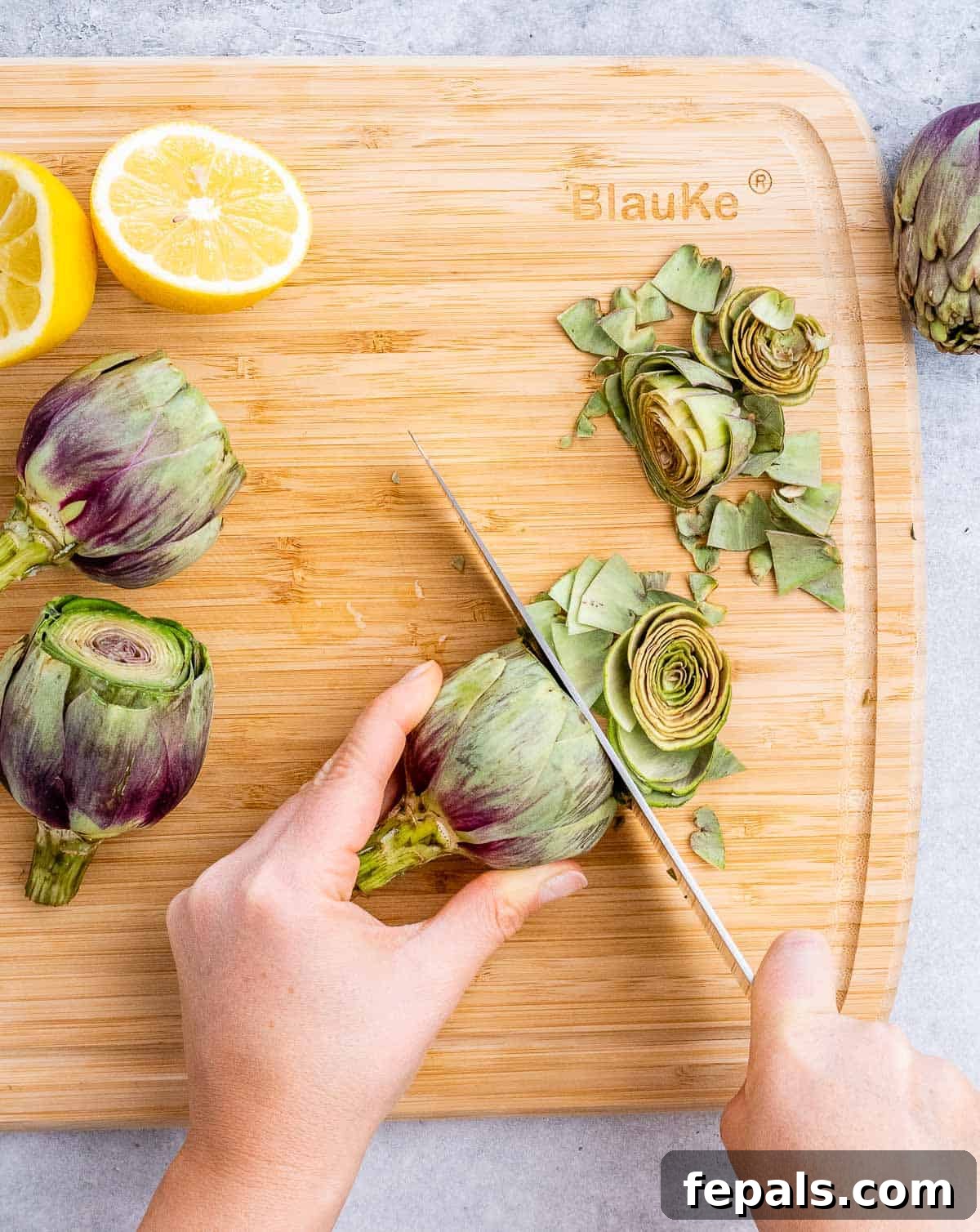 Smoky Grilled Artichoke Halves 4 A sharp knife carefully trims the spiky top portion off a fresh artichoke, preparing it for cooking.