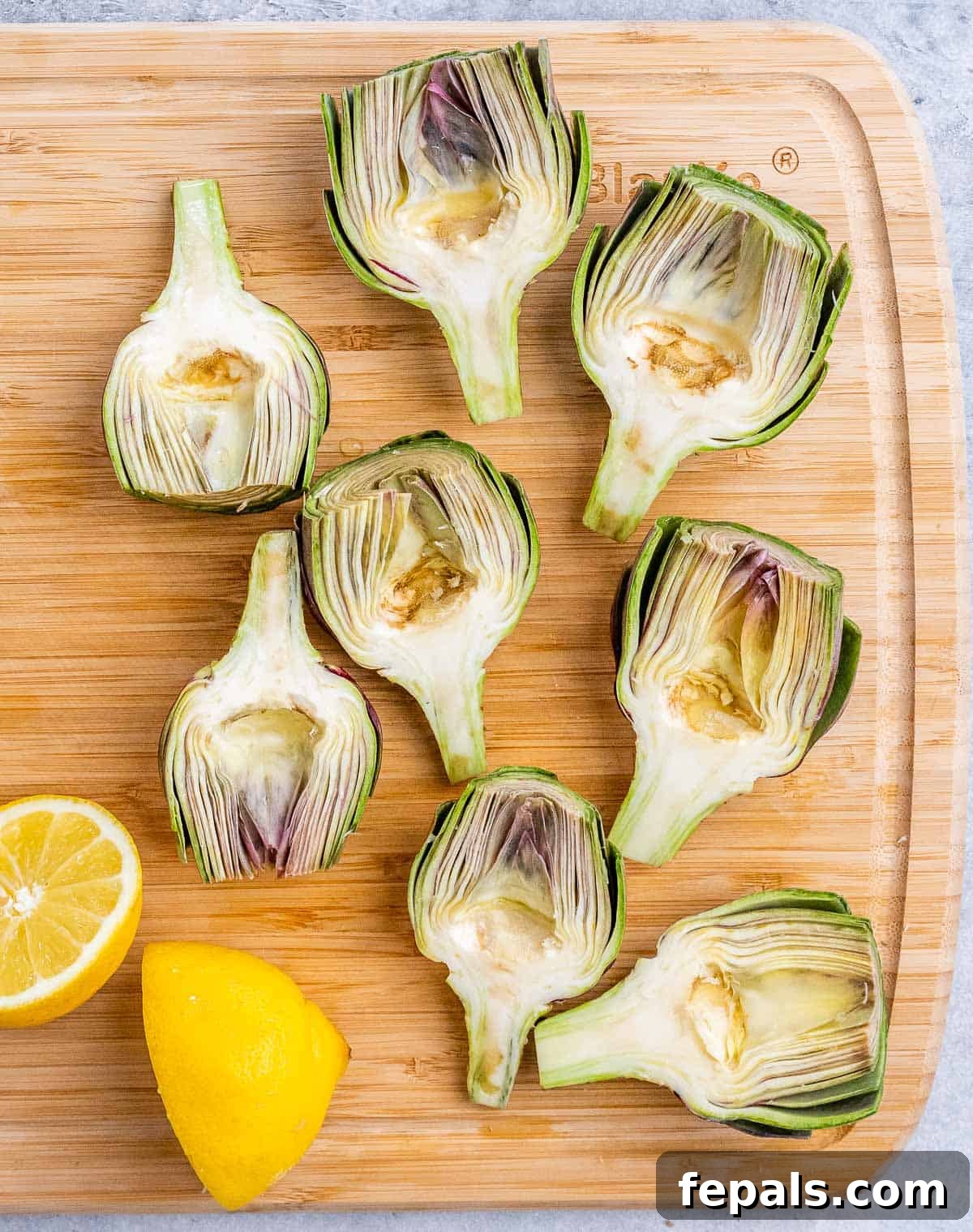 Smoky Grilled Artichoke Halves 6 Several artichokes, perfectly cut in half lengthwise, revealing their intricate internal structure, lie neatly on a wooden cutting board.
