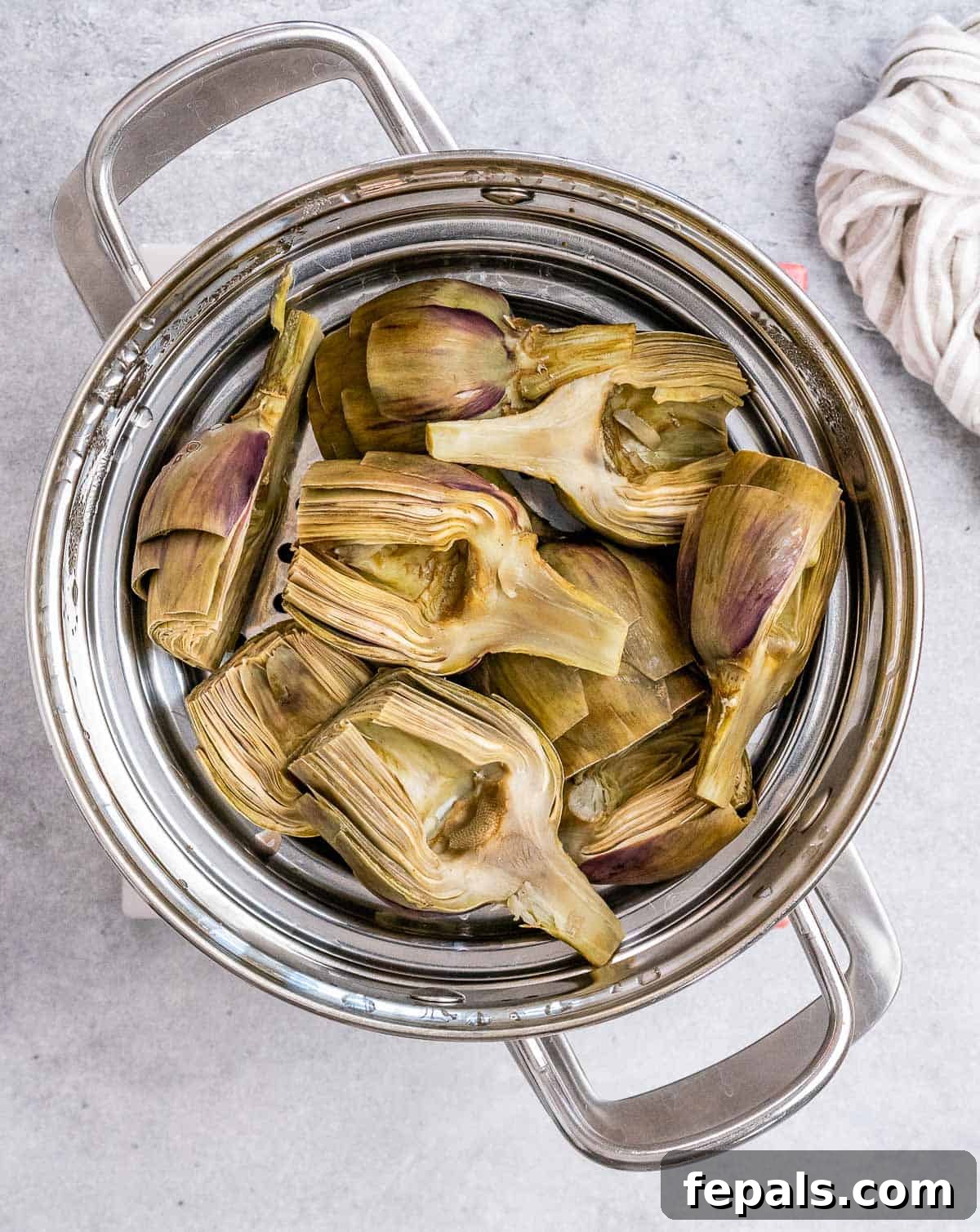 Smoky Grilled Artichoke Halves 7 Prepared artichoke halves, ready for cooking, carefully arranged within a steamer basket set above simmering water in a large pot.