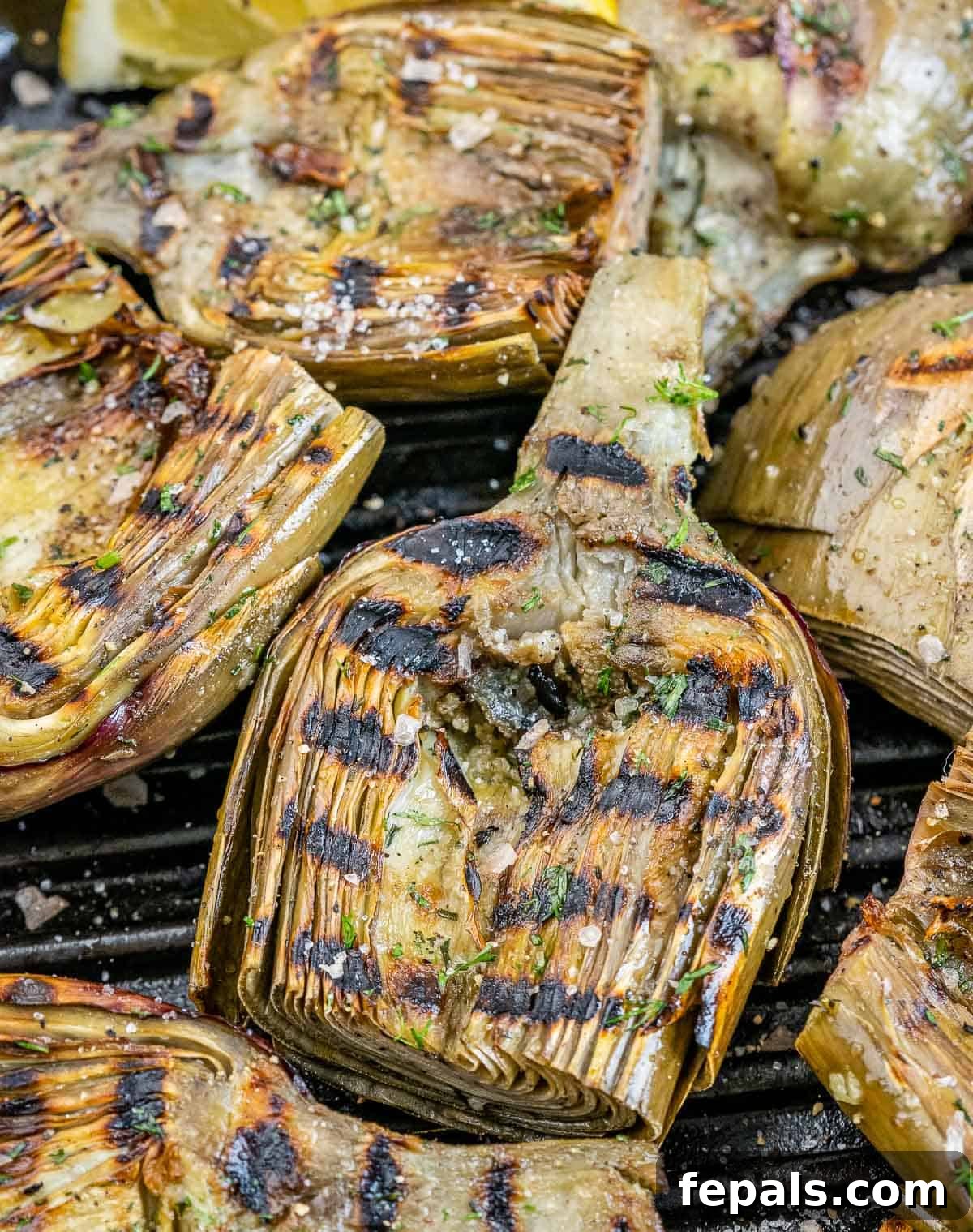 Smoky Grilled Artichoke Halves 9 Close-up of perfectly grilled artichoke halves with prominent char marks, resting on a hot grill grate.