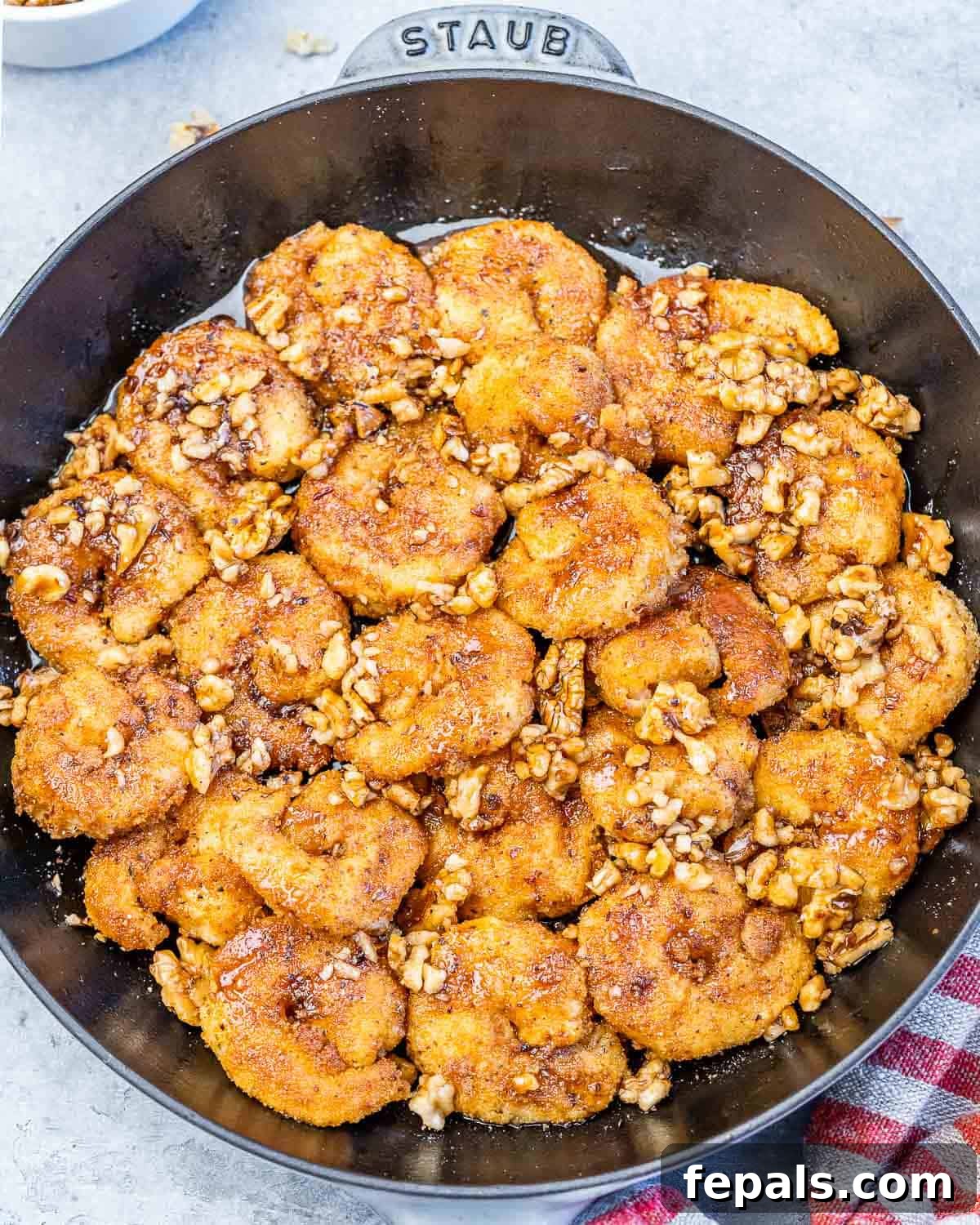A black skillet filled with perfectly golden-brown, crispy honey walnut shrimp, garnished with chopped walnuts.