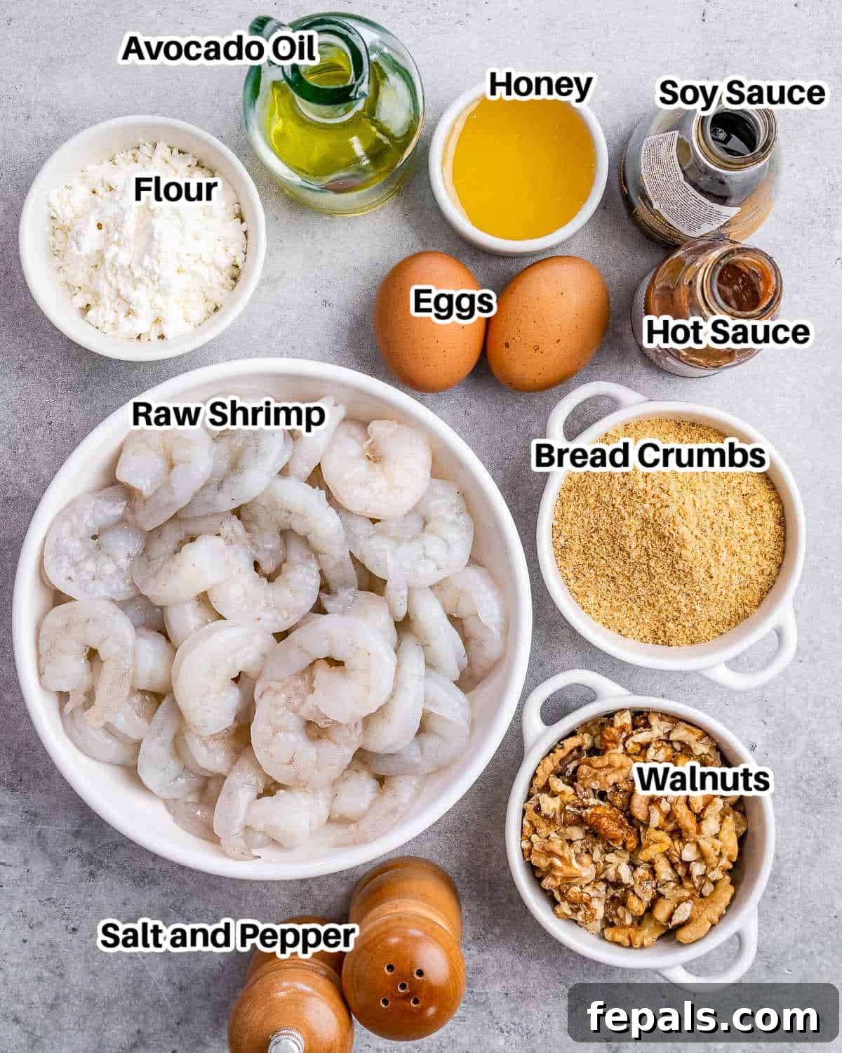 A selection of ingredients neatly arranged for making honey walnut shrimp, including fresh shrimp, flour, eggs, breadcrumbs, honey, soy sauce, hot sauce, and walnuts.