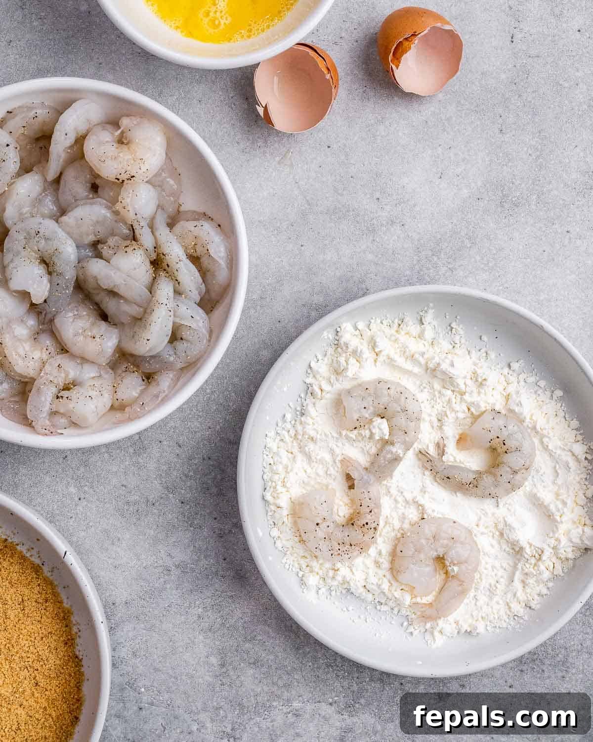 A close-up image showing raw shrimp being tossed in a bowl of flour, ready for breading.