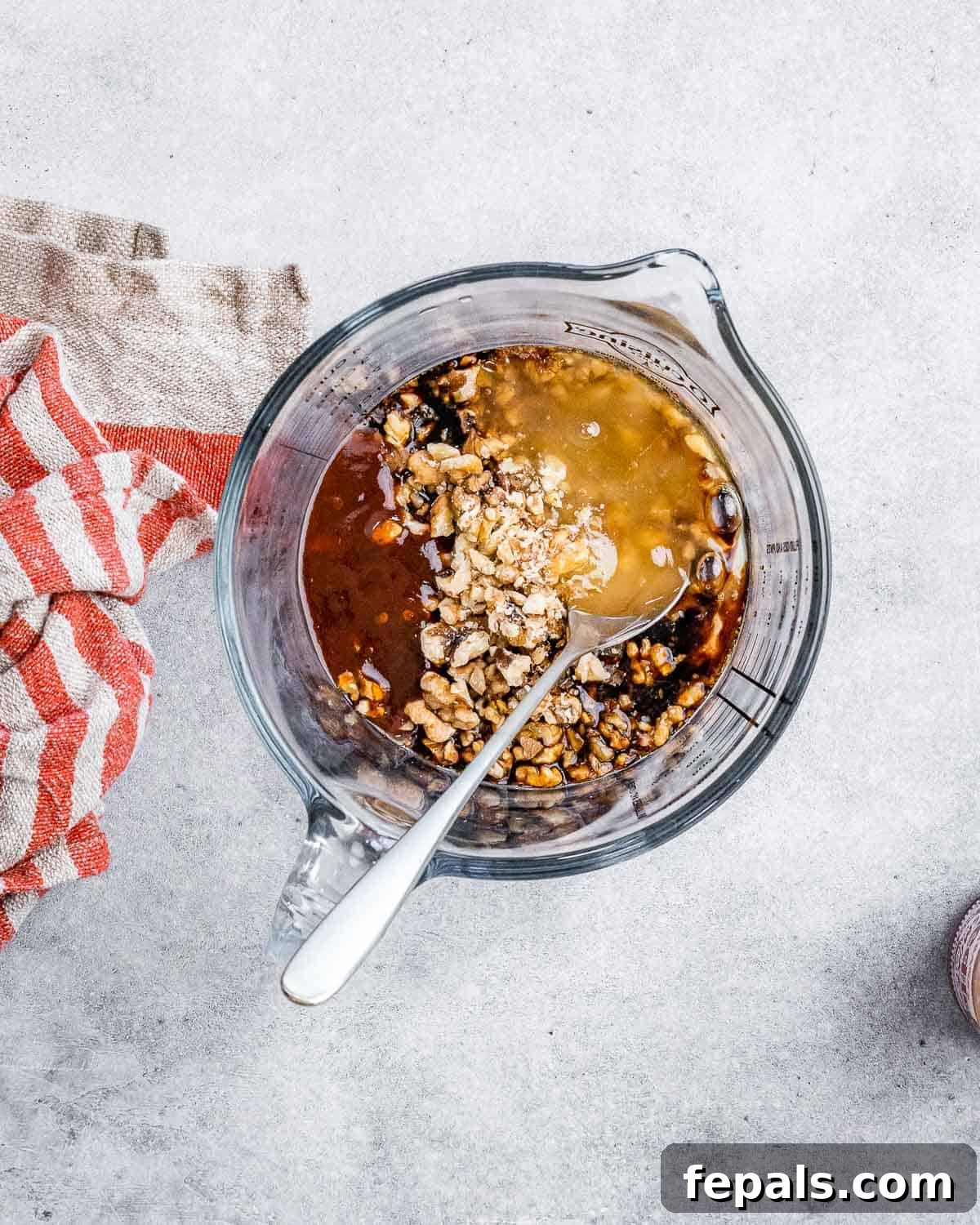 A small bowl showing honey, soy sauce, hot sauce, and chopped walnuts being whisked together to form the signature sauce.